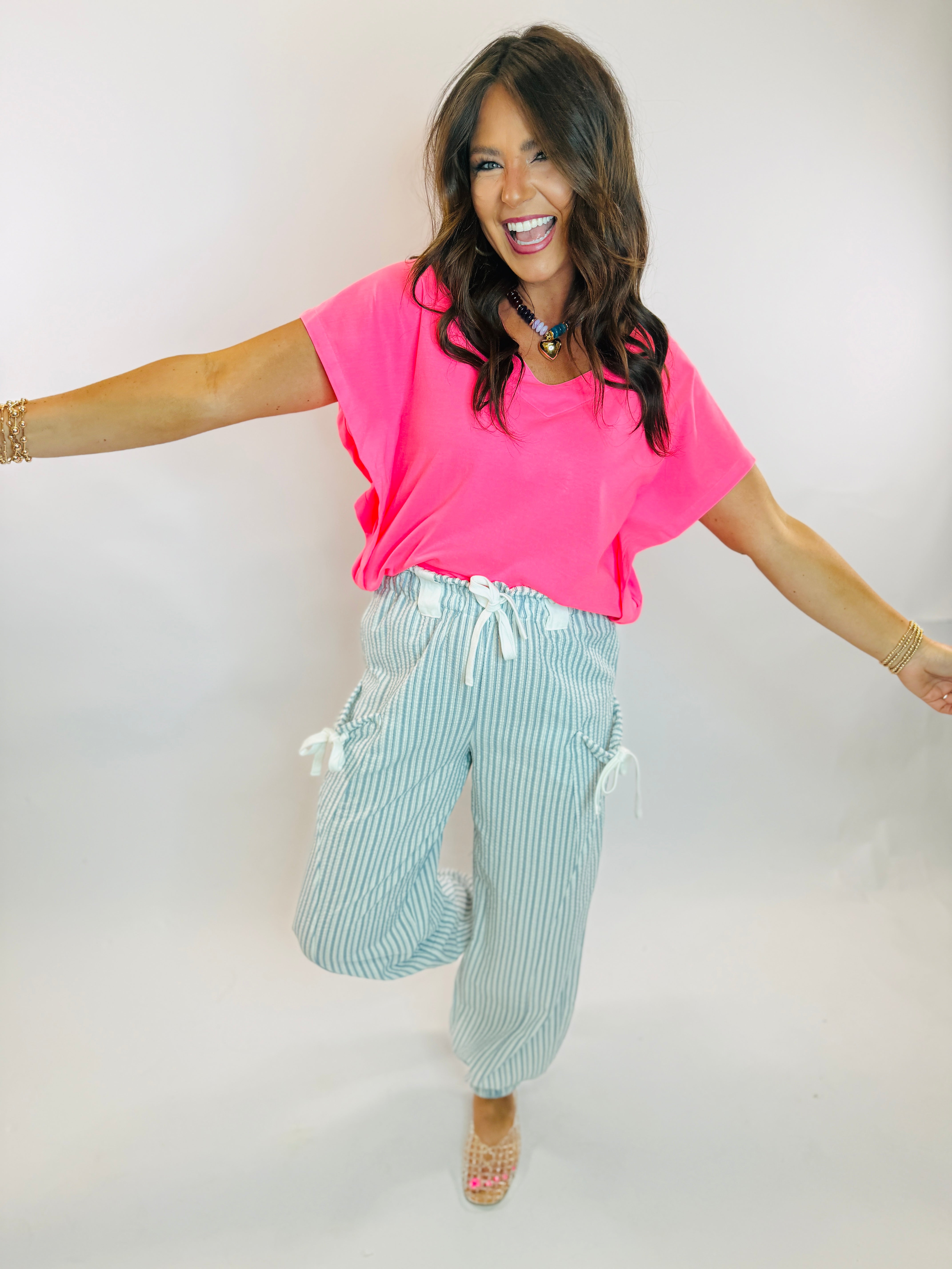 Woman wearing a bright neon pink short-sleeve V-neck top paired with striped drawstring pants.
