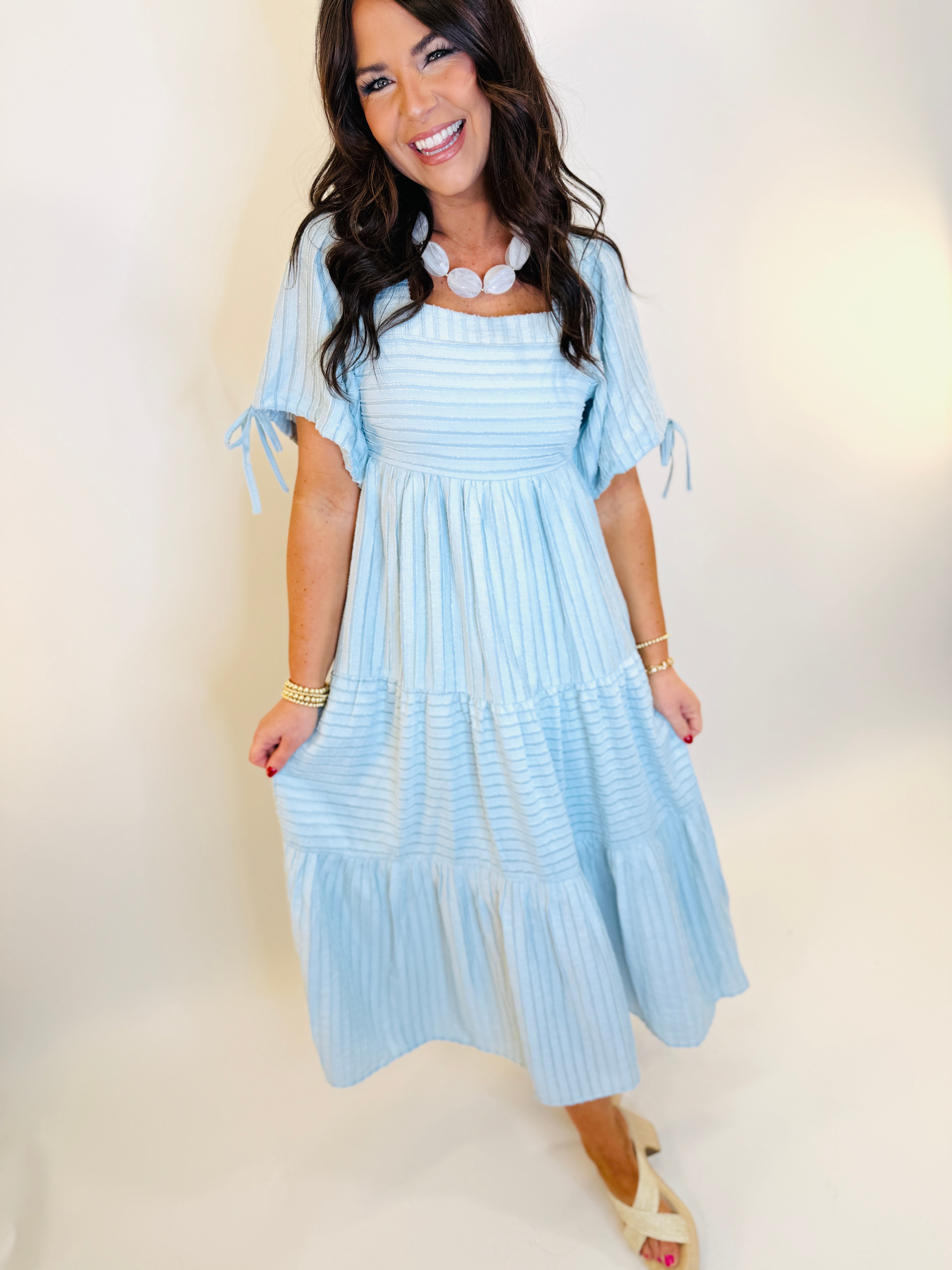 Woman wearing light blue striped tiered maxi dress with short tie sleeves and smocked bodice