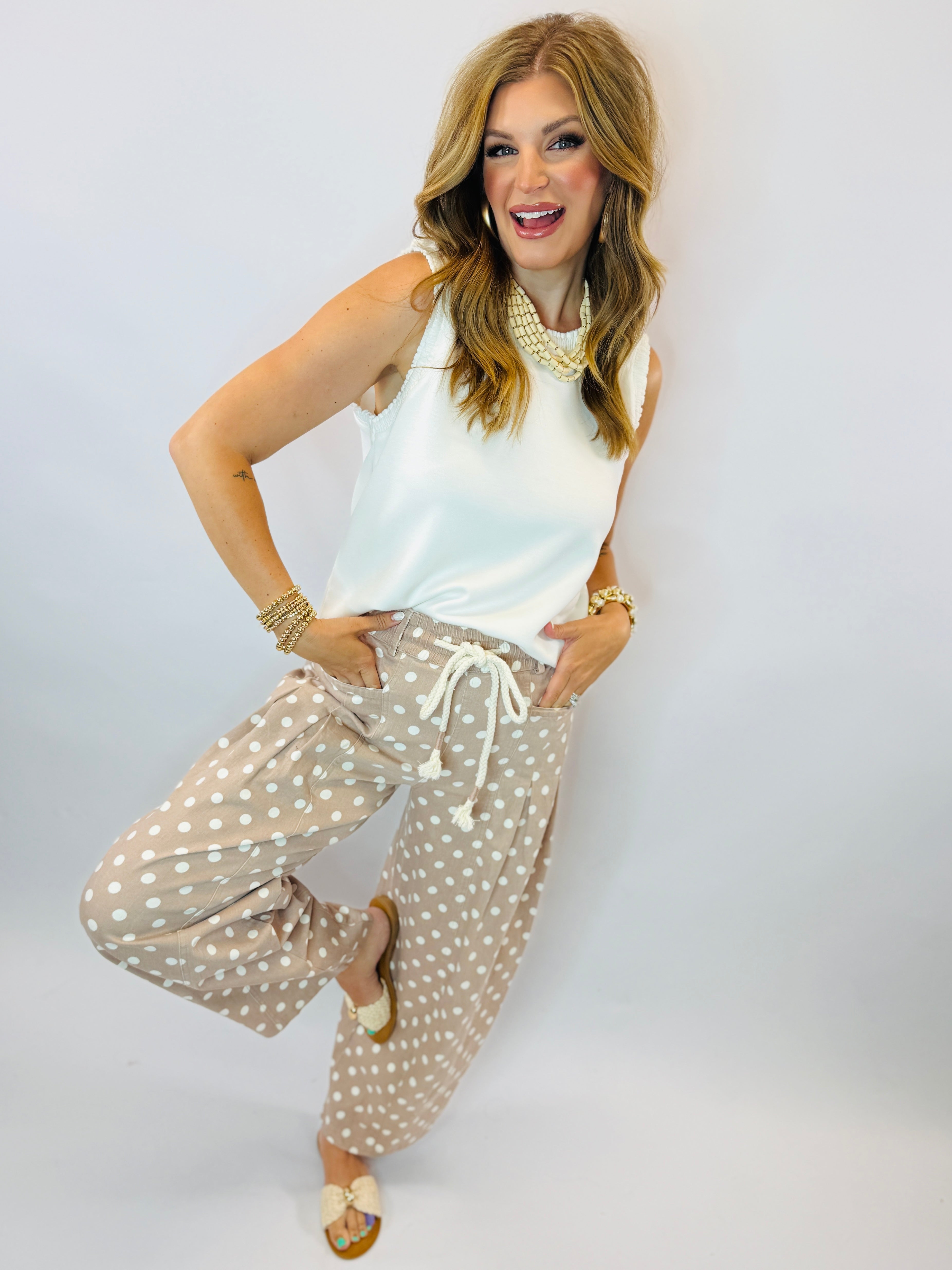 Woman wearing white sleeveless top and beige polka dot drawstring barrel pants with pearl necklace and bracelets