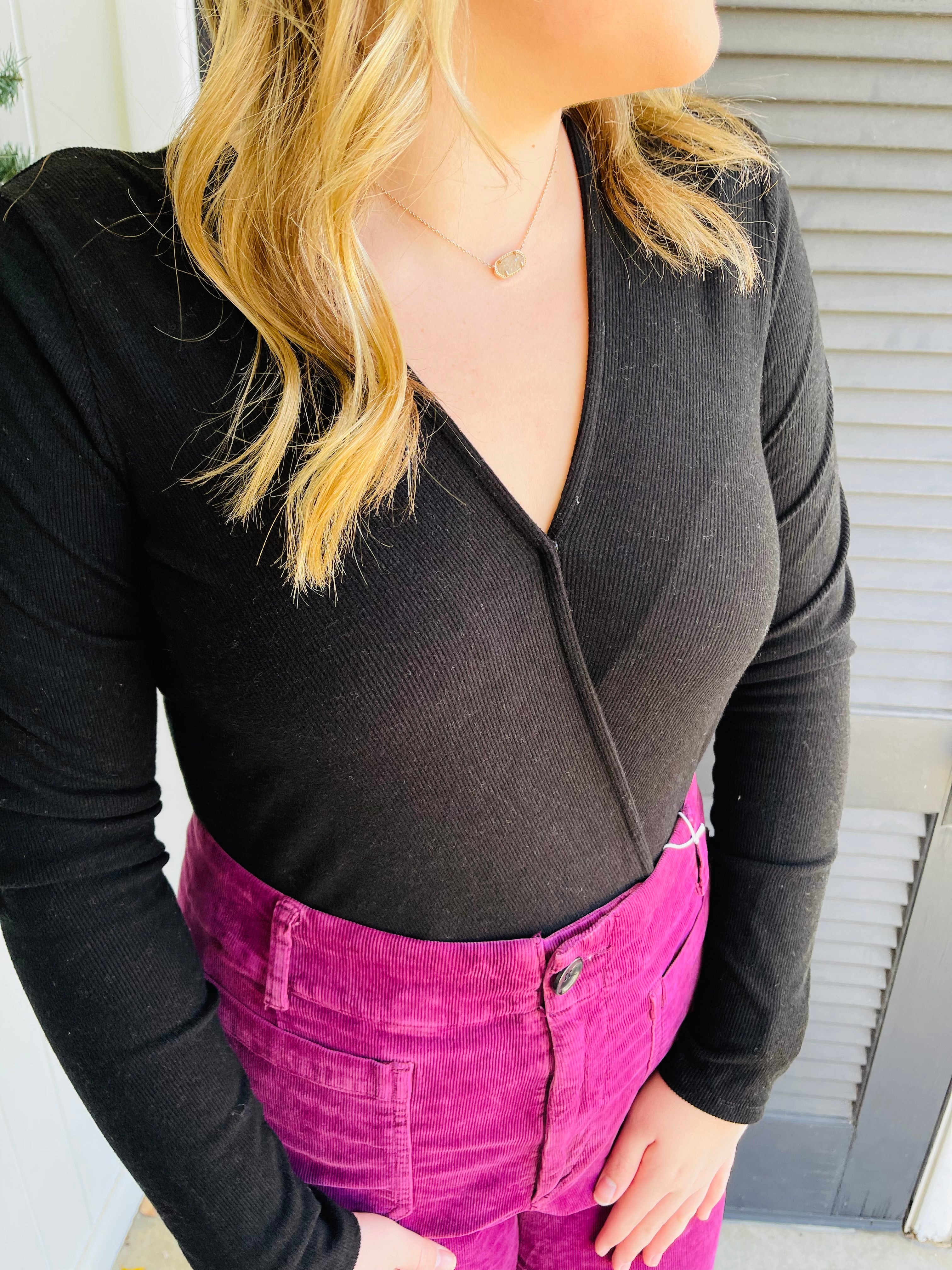 Woman wearing black ribbed long-sleeve top and bright pink corduroy high-waisted pants