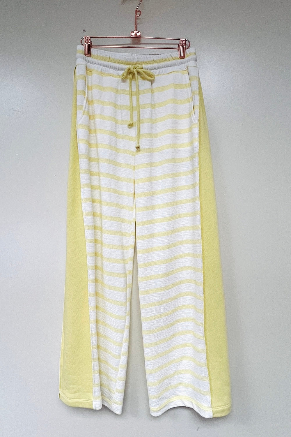 Yellow and white striped wide-leg drawstring pants with solid yellow side panels hanging on rose gold hanger