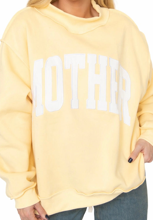 Yellow oversized mock neck sweatshirt with white "MOTHER" text worn with jeans