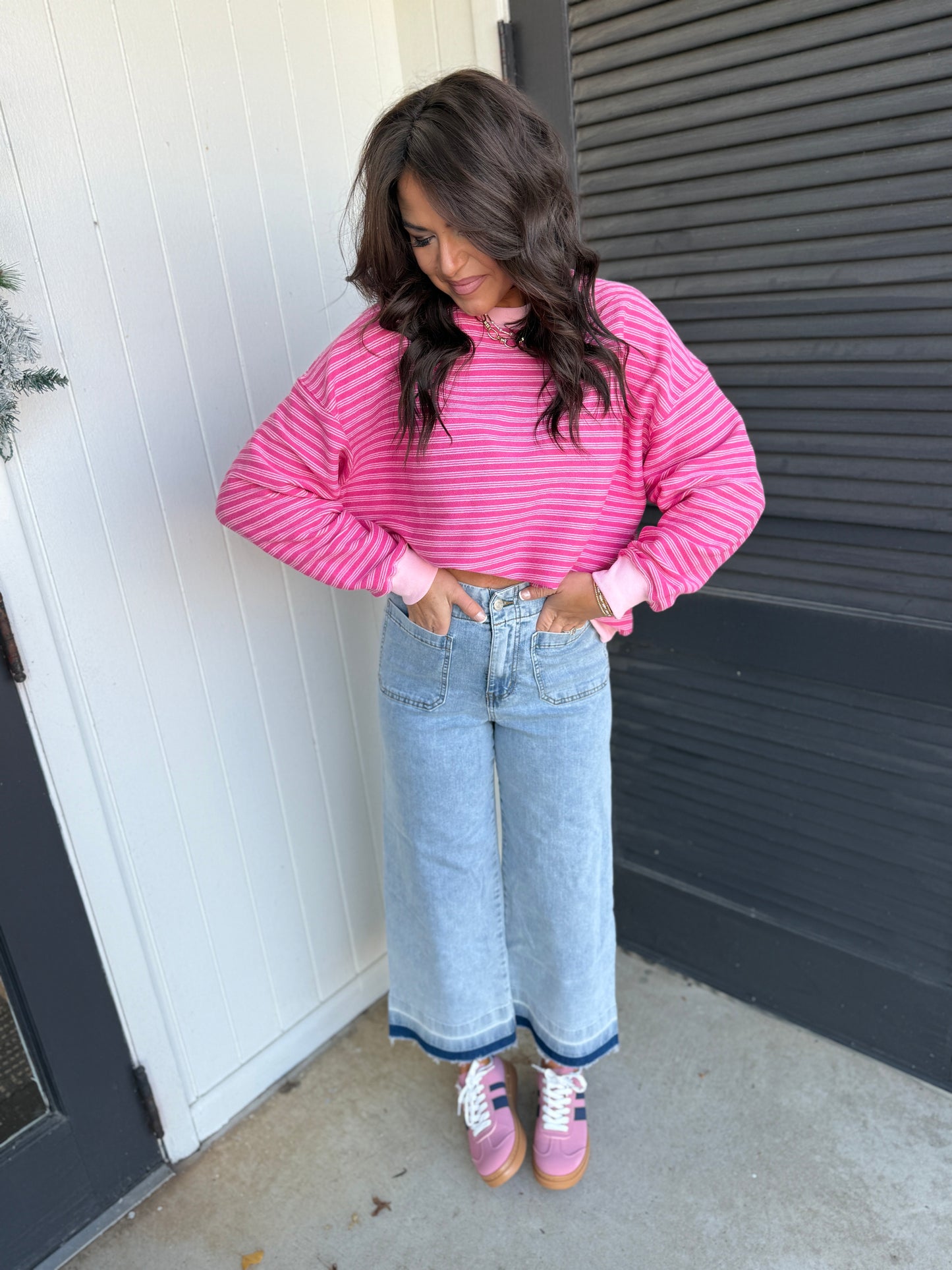 Woman wearing light blue wide-leg Jana jeans with raw hem detail, paired with pink striped top and sneakers.