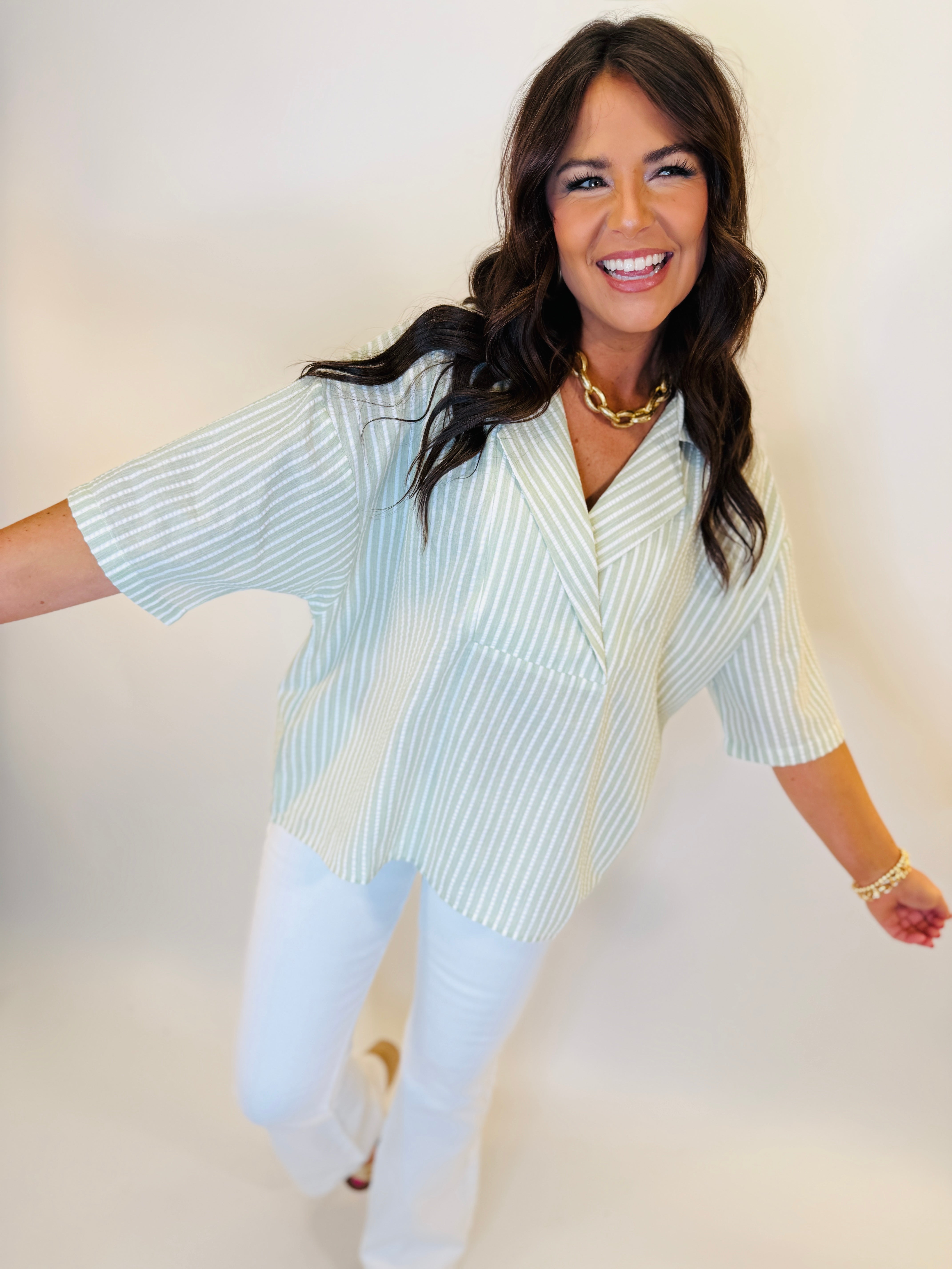 Woman wearing light blue and white striped button-up shirt with three-quarter sleeves and gold chain necklace.