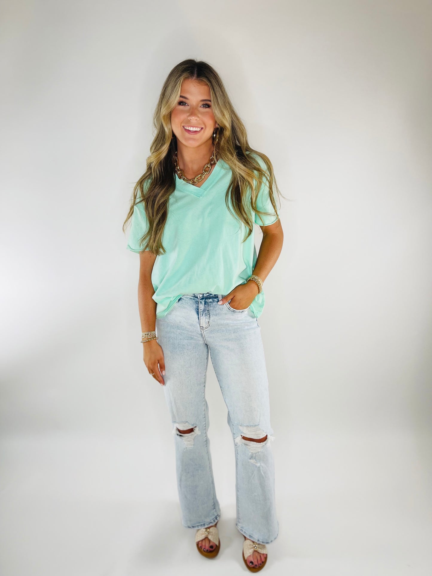 Woman wearing mint green v-neck Ailani tee with distressed light wash jeans and layered necklaces.