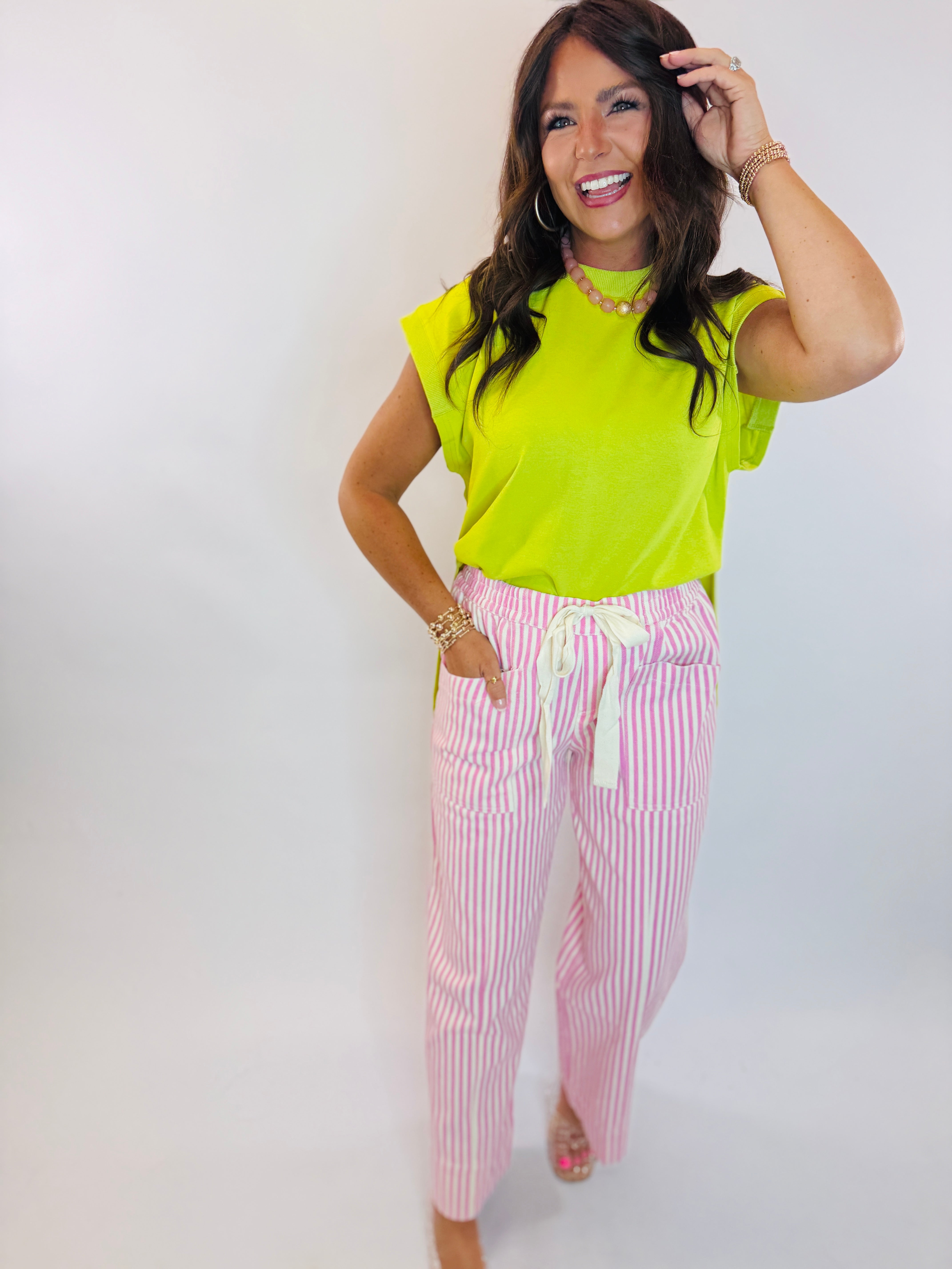 Woman wearing a bright lime green sleeveless top with padded shoulders, paired with pink striped pants.