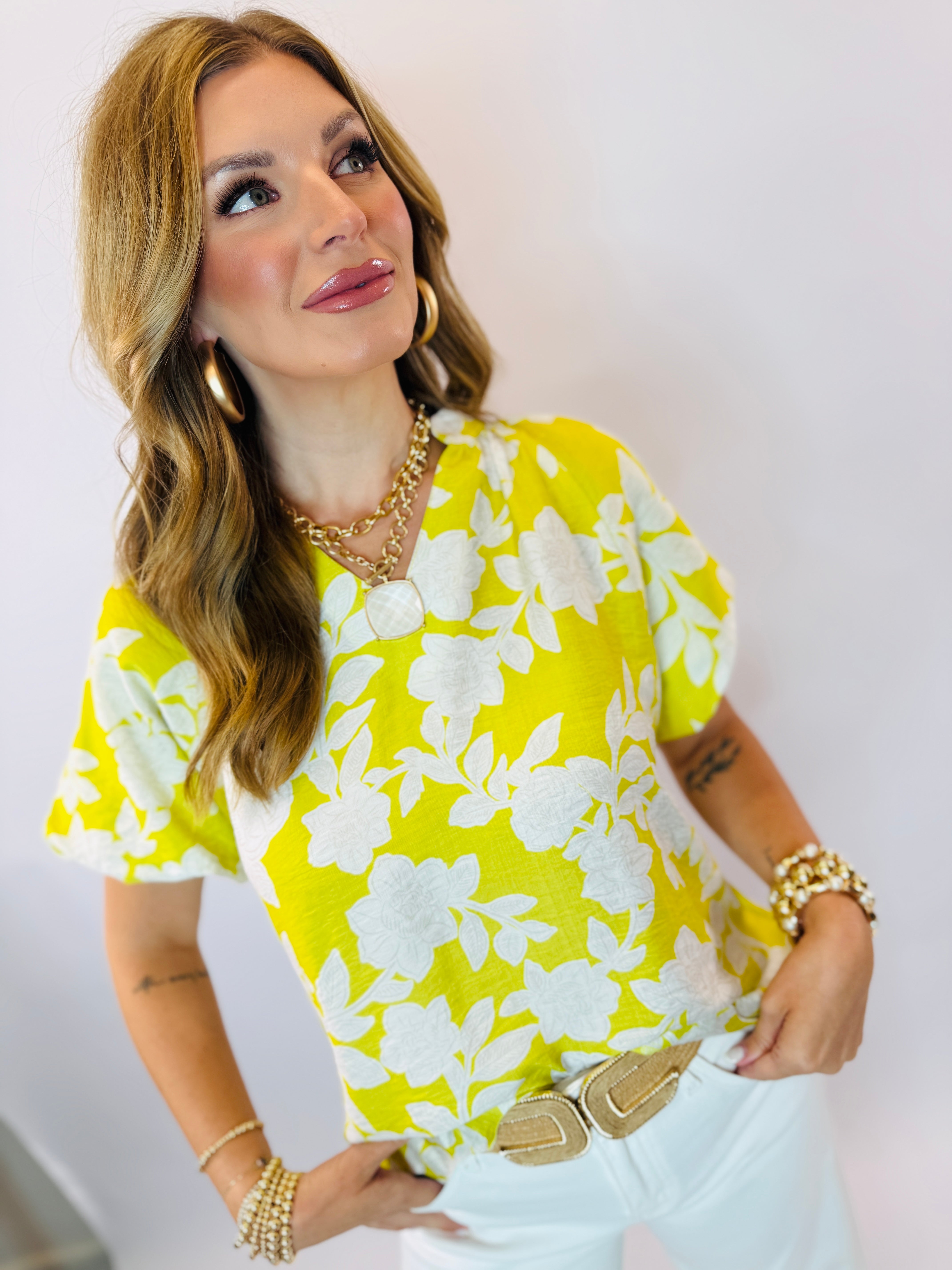 Woman wearing yellow floral print short-sleeve top with gold jewelry and layered necklaces