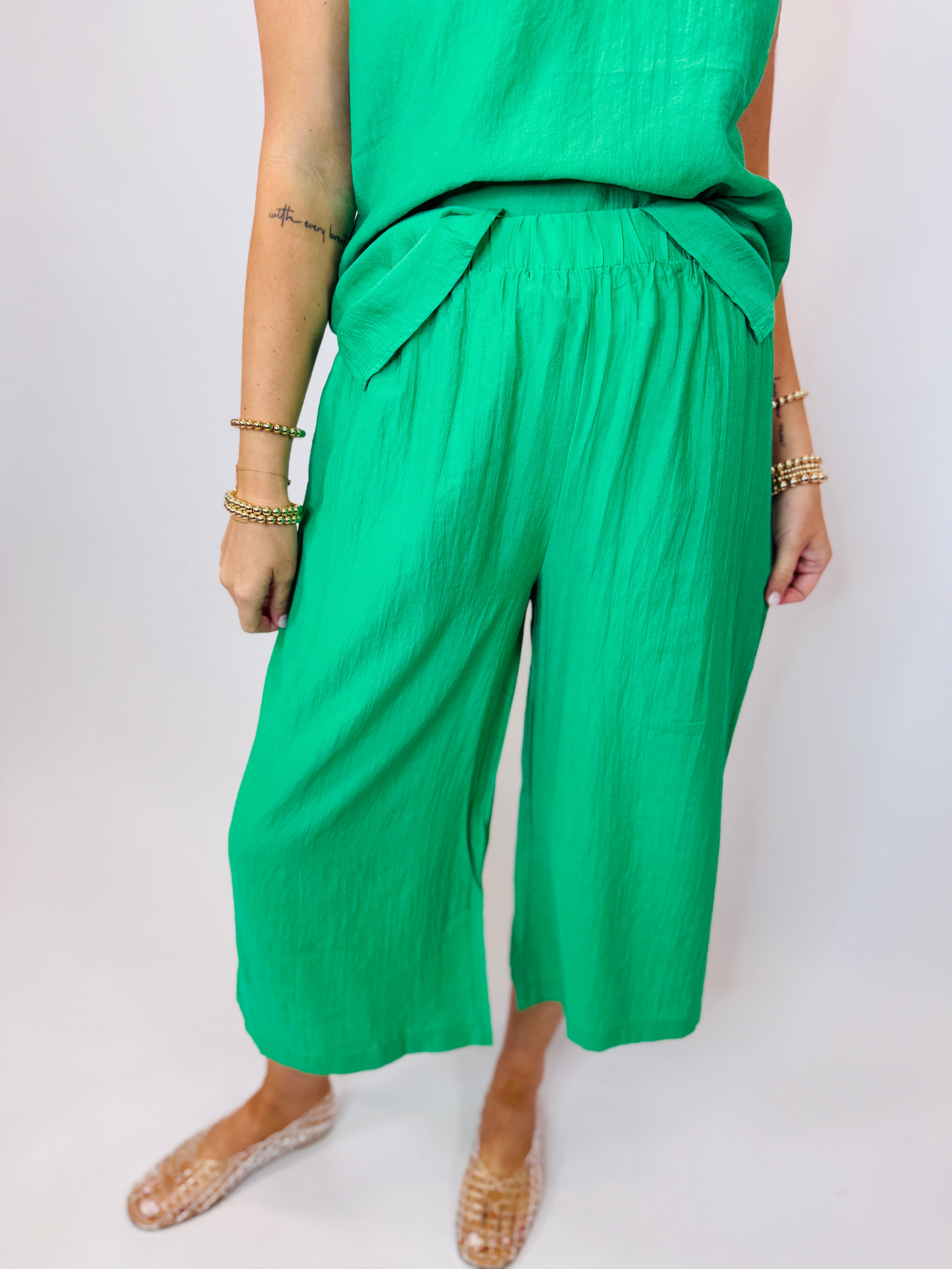 Woman wearing bright green coordinating top and wide-leg pants set with gold jewelry and woven sandals.