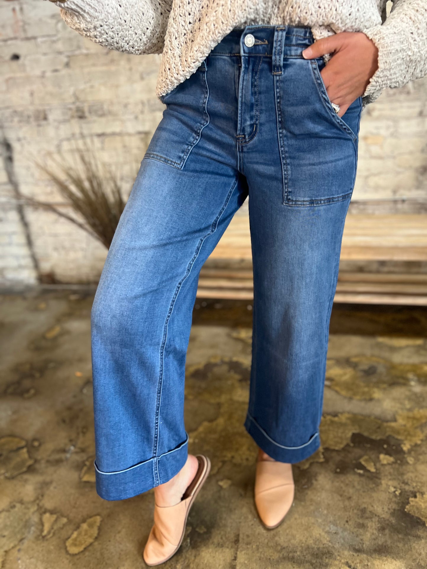 Wide-leg denim jeans with high waist, front pockets, and cuffed hems styled with cream sweater and tan flats.