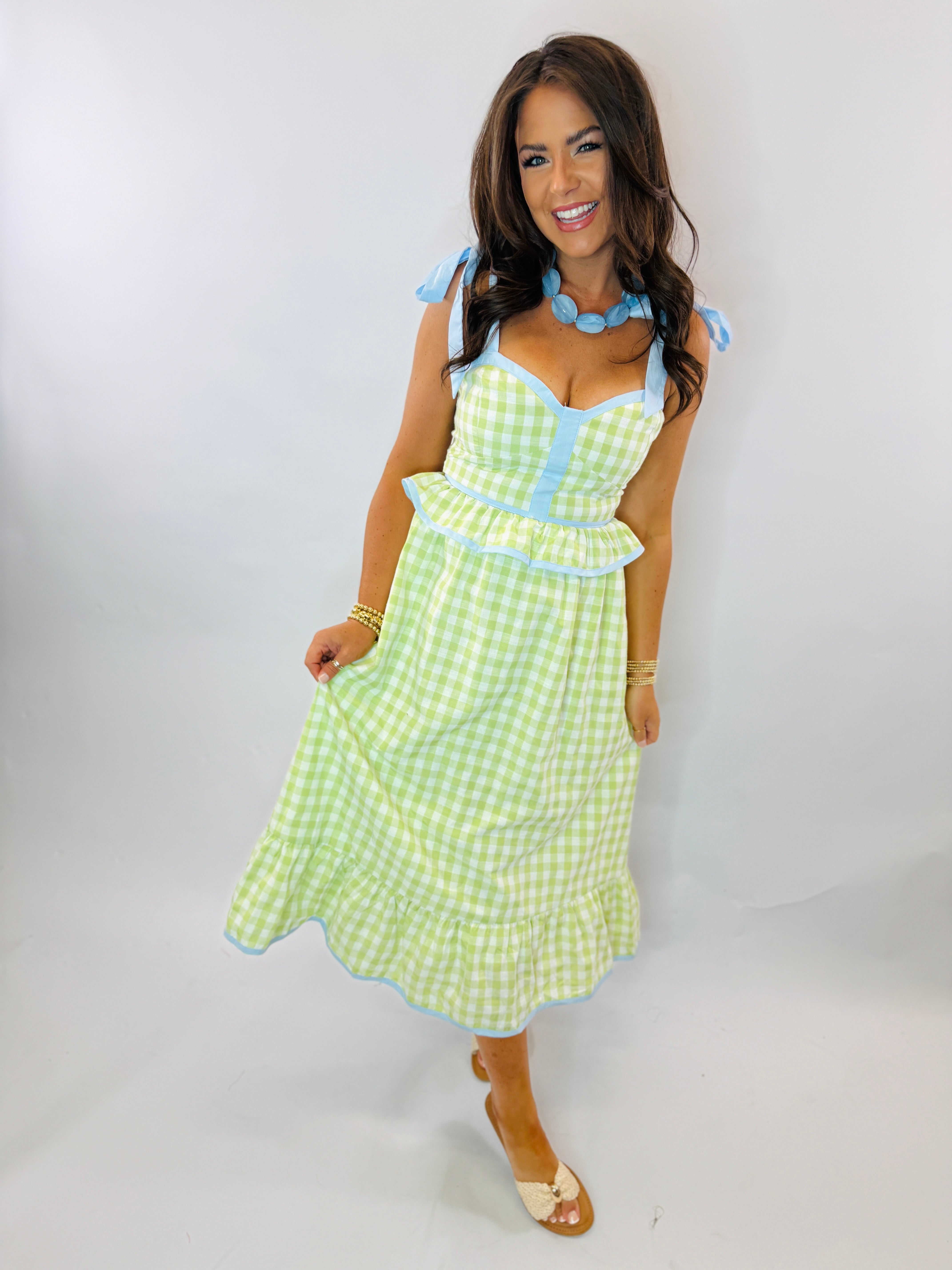 Woman wearing green gingham Grace dress with blue trim, tie straps, and sweetheart neckline