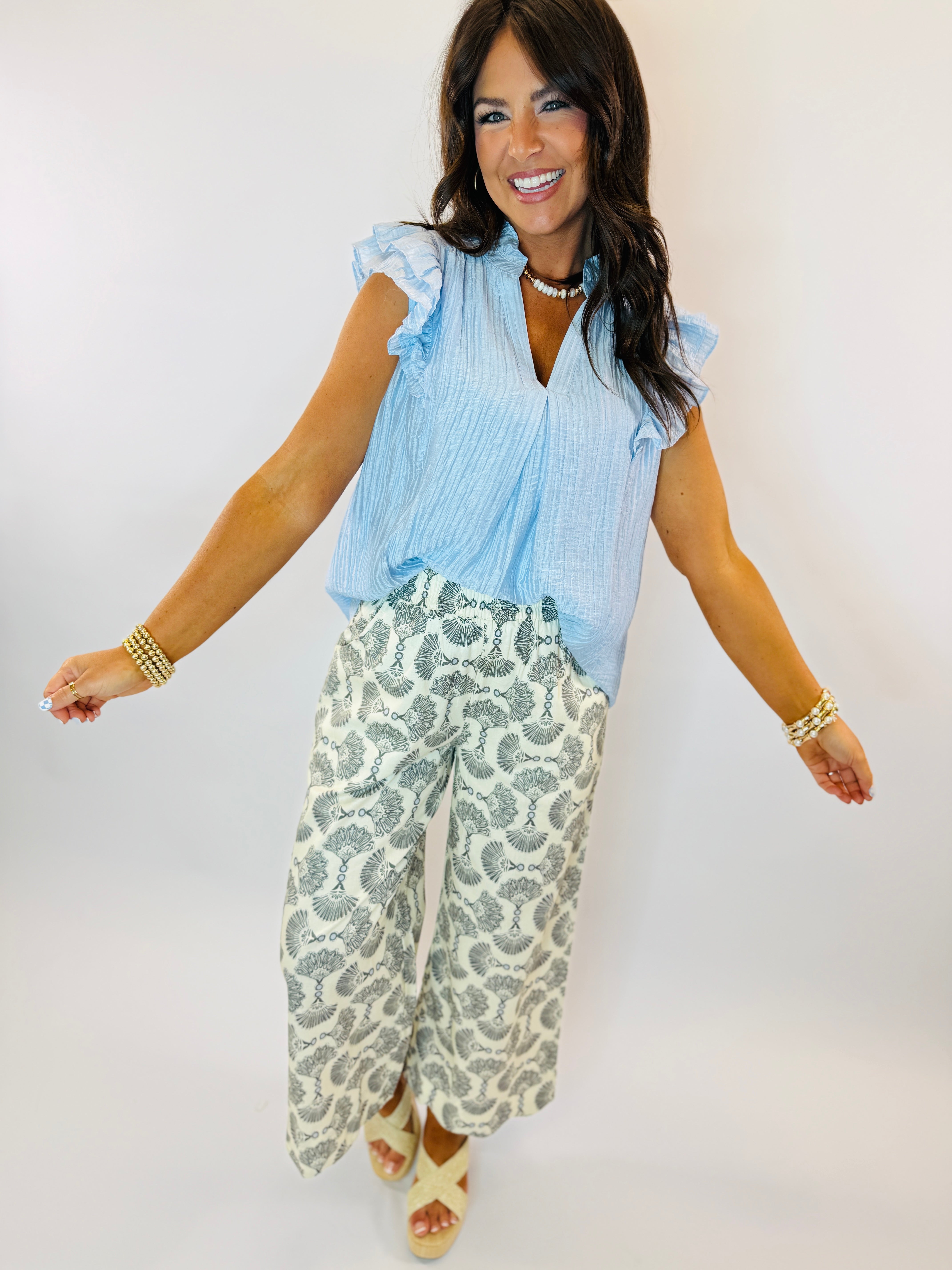 Woman wearing light blue sleeveless ruffled tank top with V-neck, paired with patterned wide-leg pants