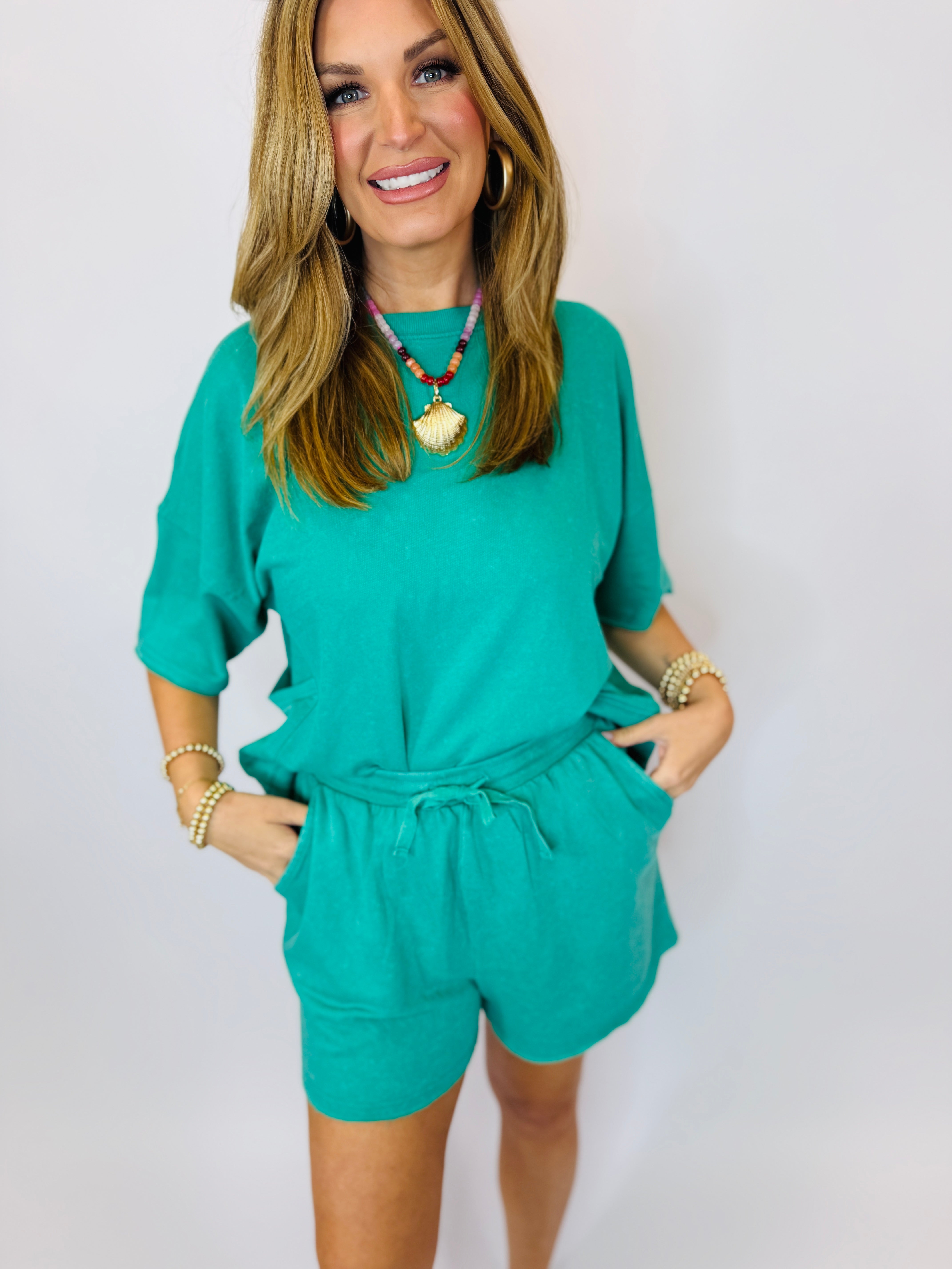 Woman wearing turquoise two-piece matching set with drawstring shorts and three-quarter sleeve top, styled with colorful b...