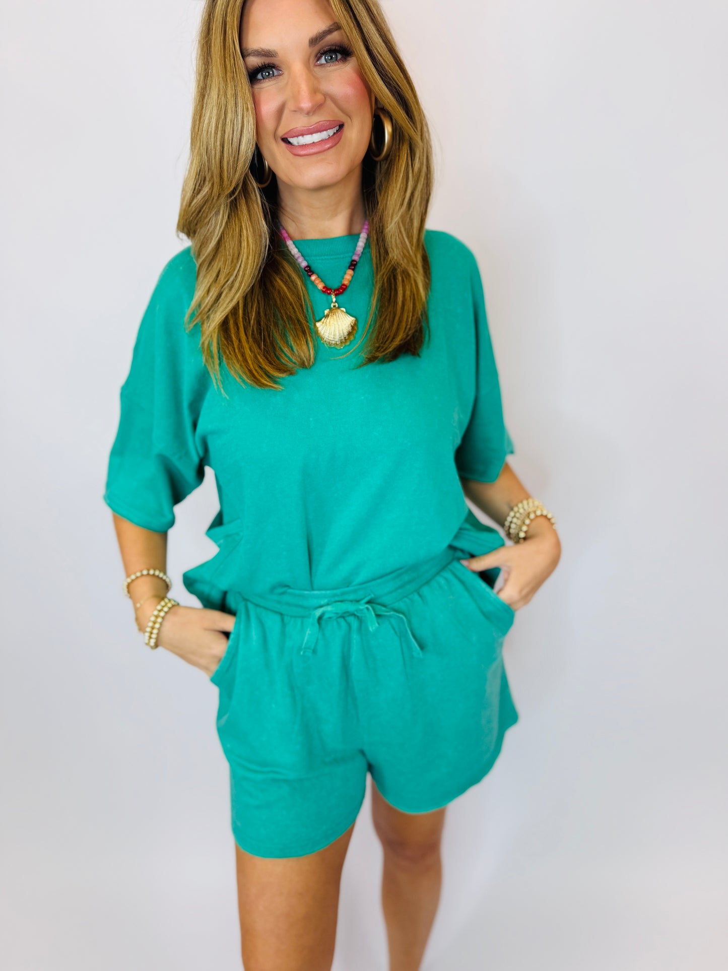 Woman wearing turquoise two-piece matching set with drawstring shorts and three-quarter sleeve top, styled with colorful b...