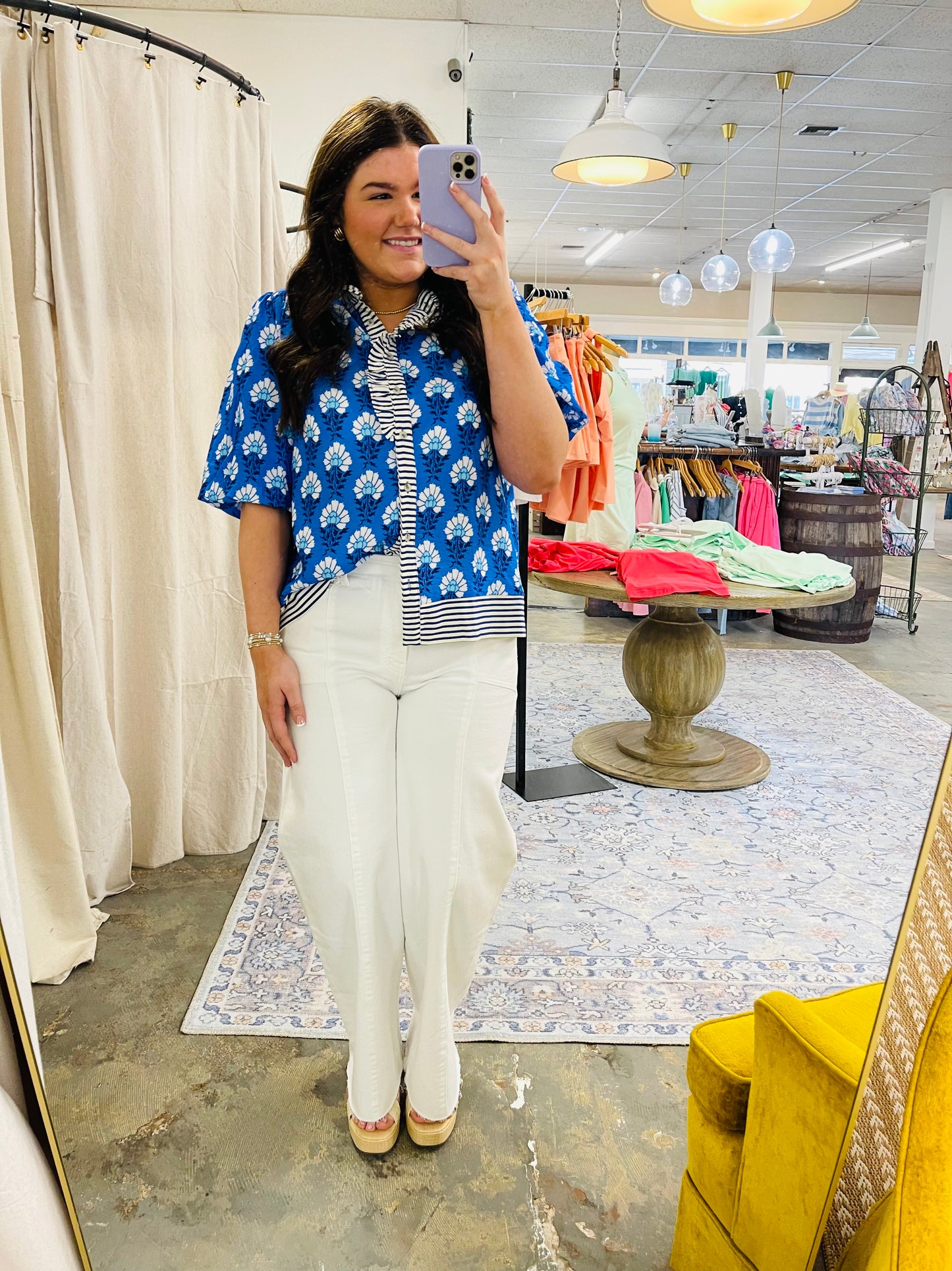 Woman wearing blue floral short-sleeve top with striped collar, white pants, and platform sandals in clothing store