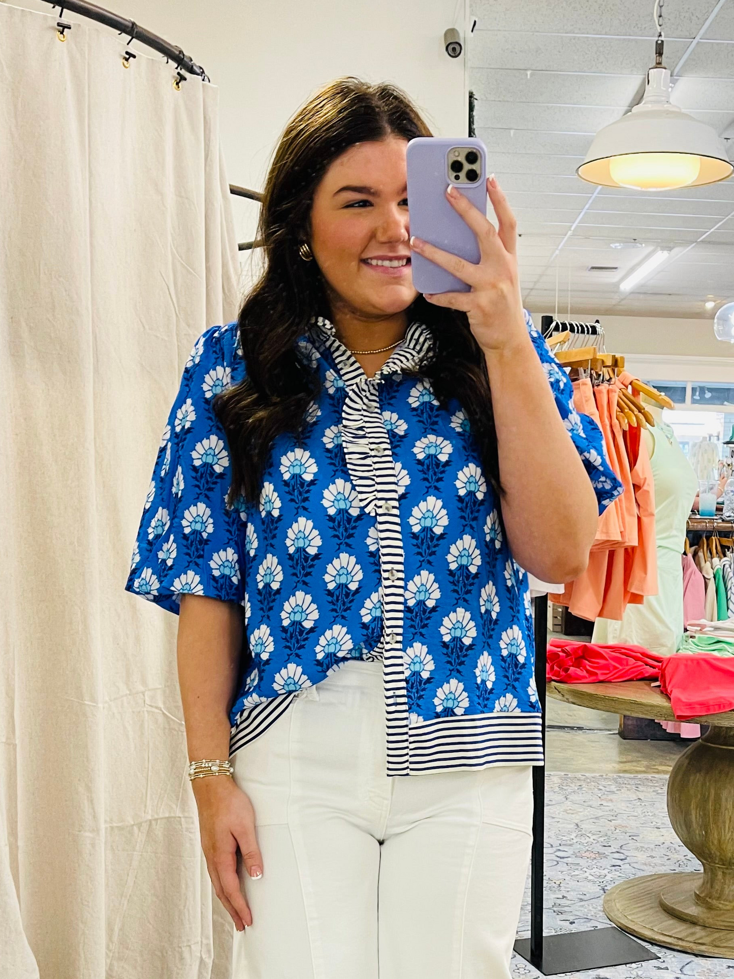 Woman wearing blue floral print short-sleeve top with striped undershirt, taking mirror selfie in clothing store