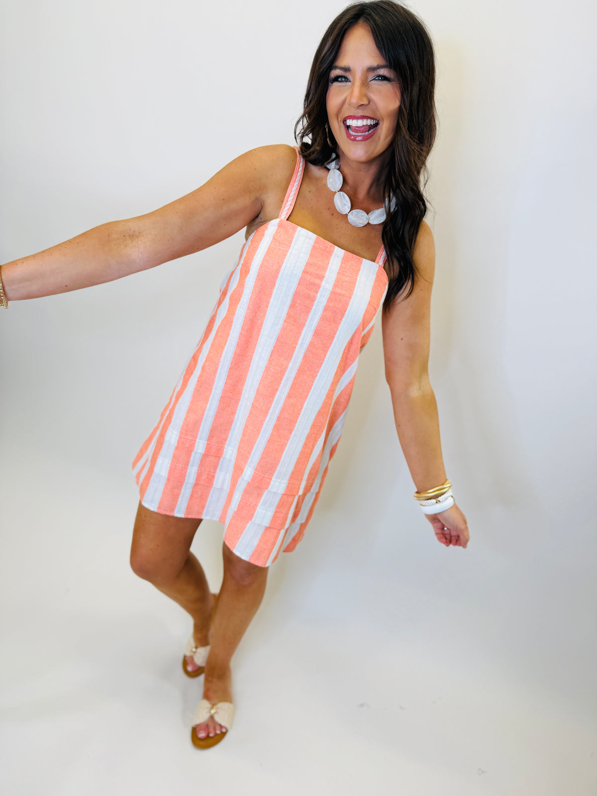 Woman wearing coral and white striped one-shoulder asymmetrical dress with statement necklace and sandals