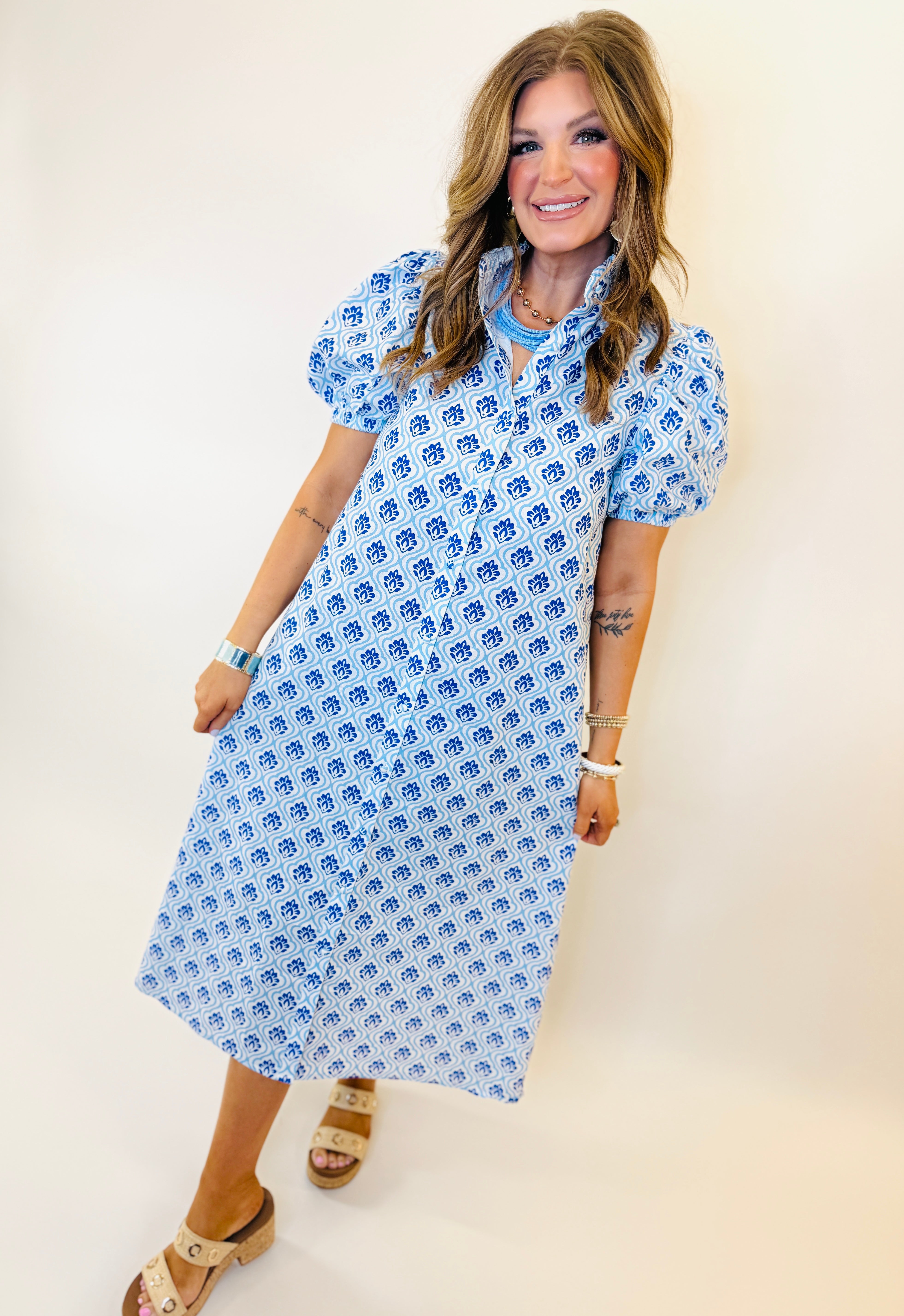 Woman wearing blue and white patterned Tessa dress with short sleeves and midi length, styled with tan sandals.