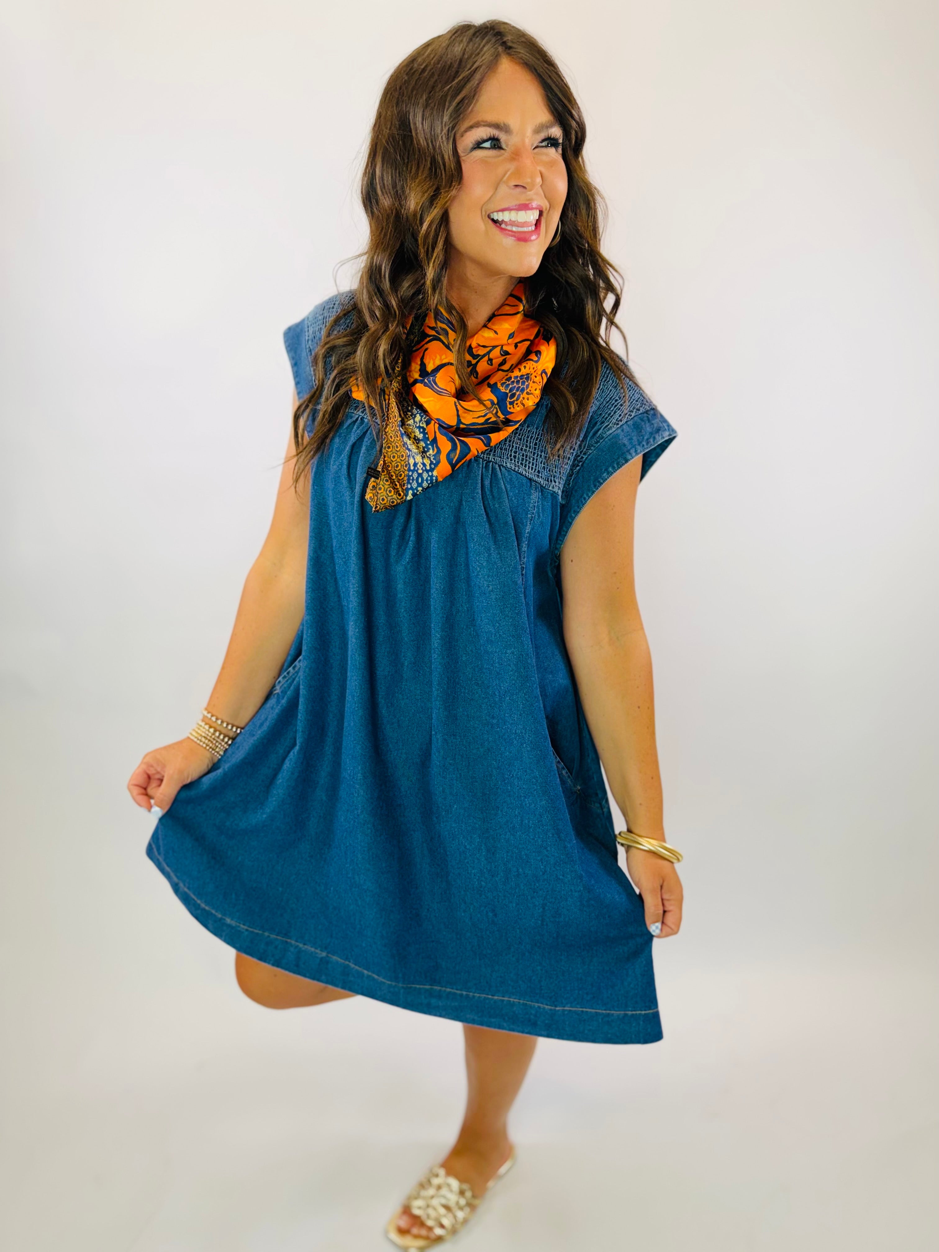 Woman wearing Carson Dress in medium wash denim with orange floral scarf, gold bracelets, and white sandals.