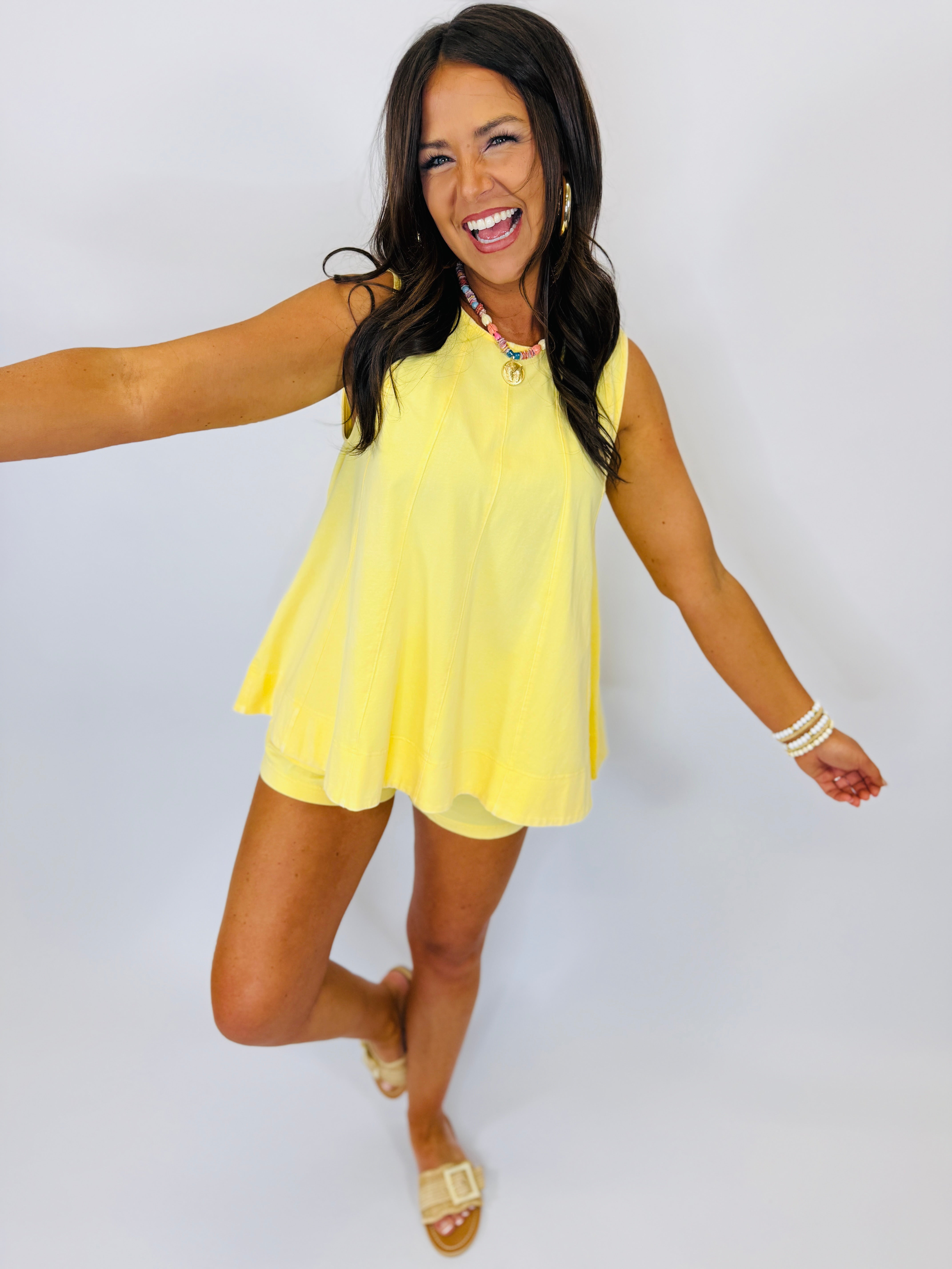 Woman wearing bright yellow sleeveless Parker Set shorts outfit, smiling and posing with arms outstretched