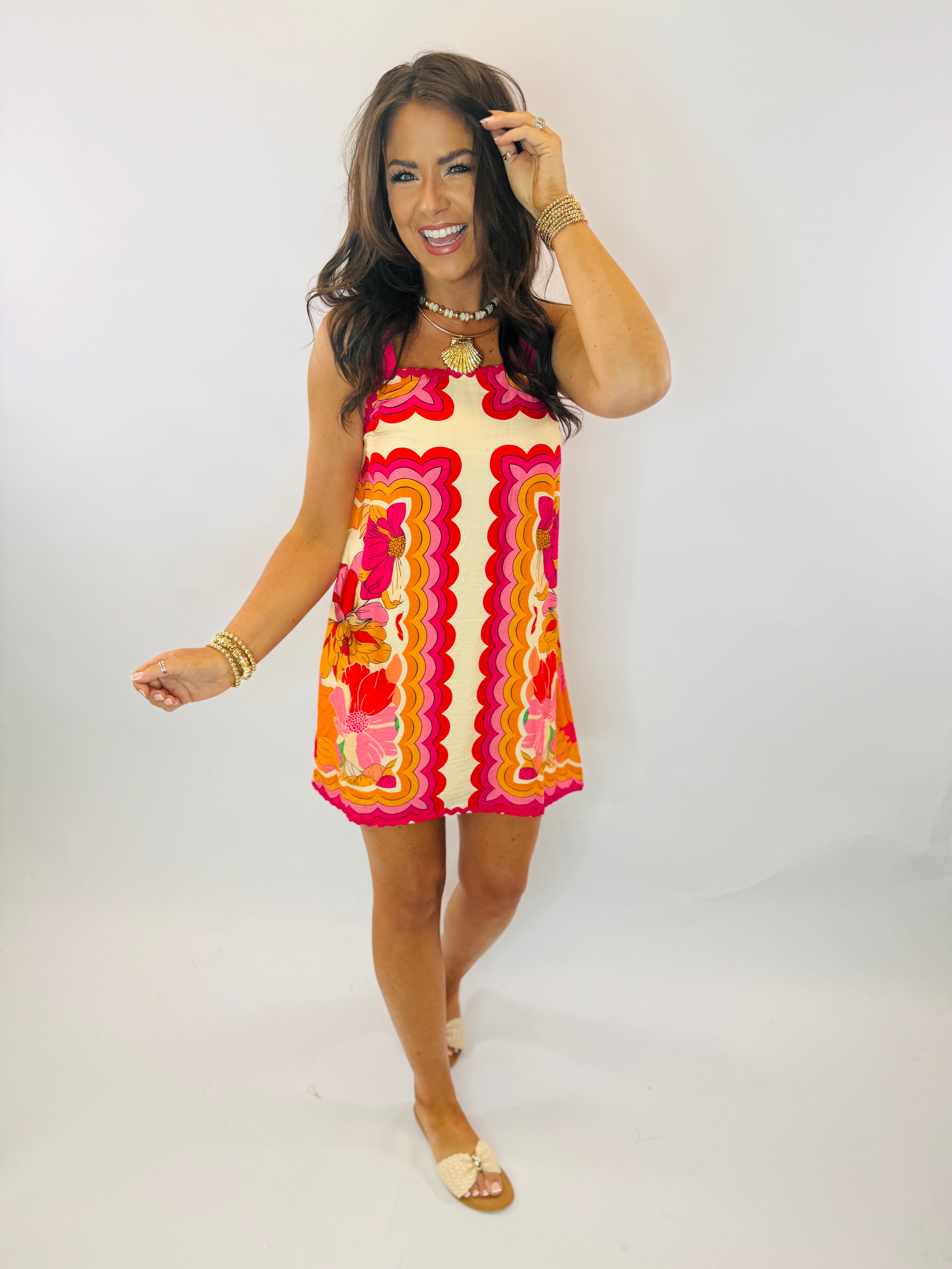 Woman wearing colorful retro-print sleeveless mini dress with vibrant pink, orange, and yellow wavy patterns.