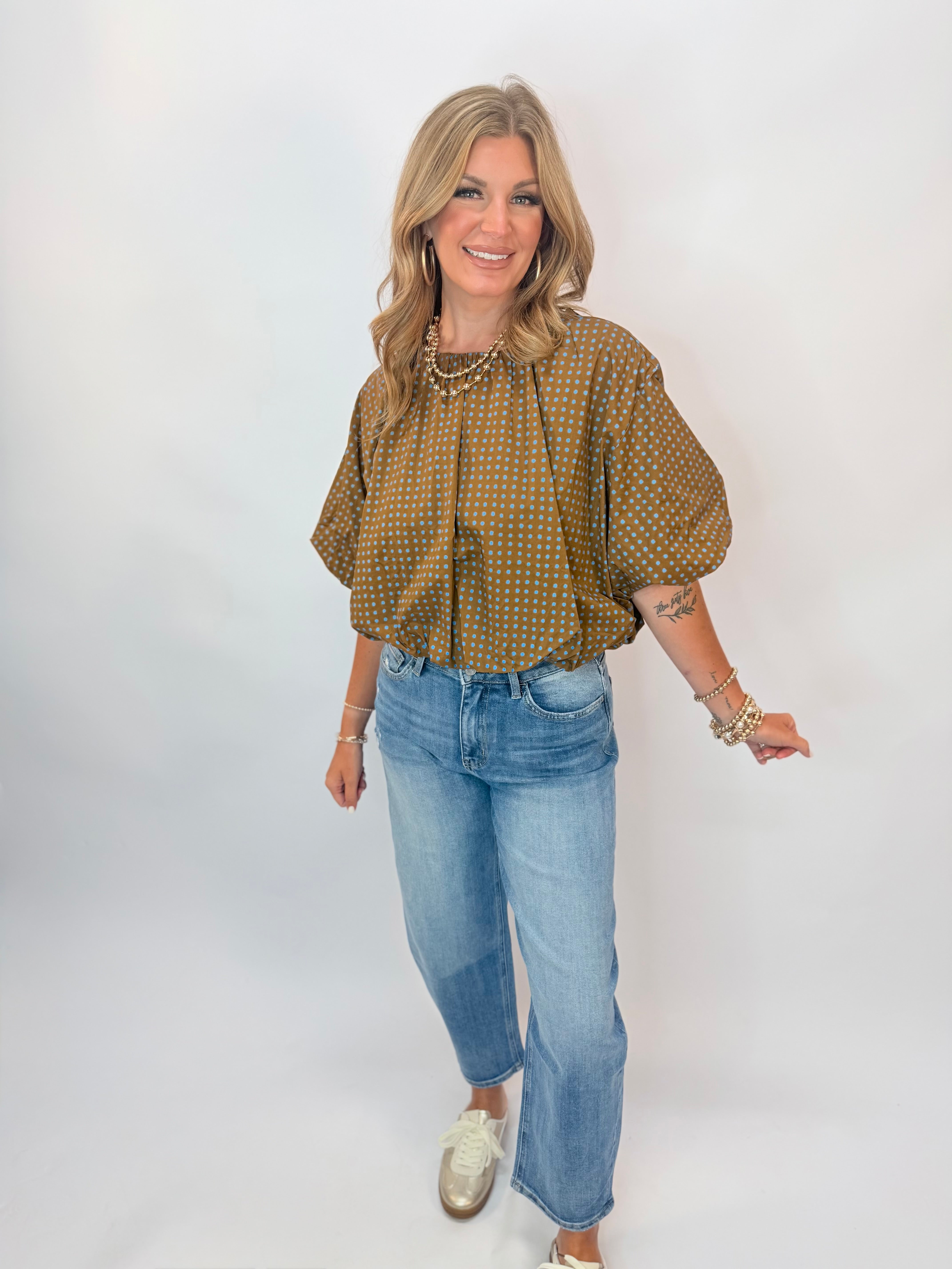 Woman wearing olive green polka dot puff sleeve blouse paired with light wash wide-leg jeans.
