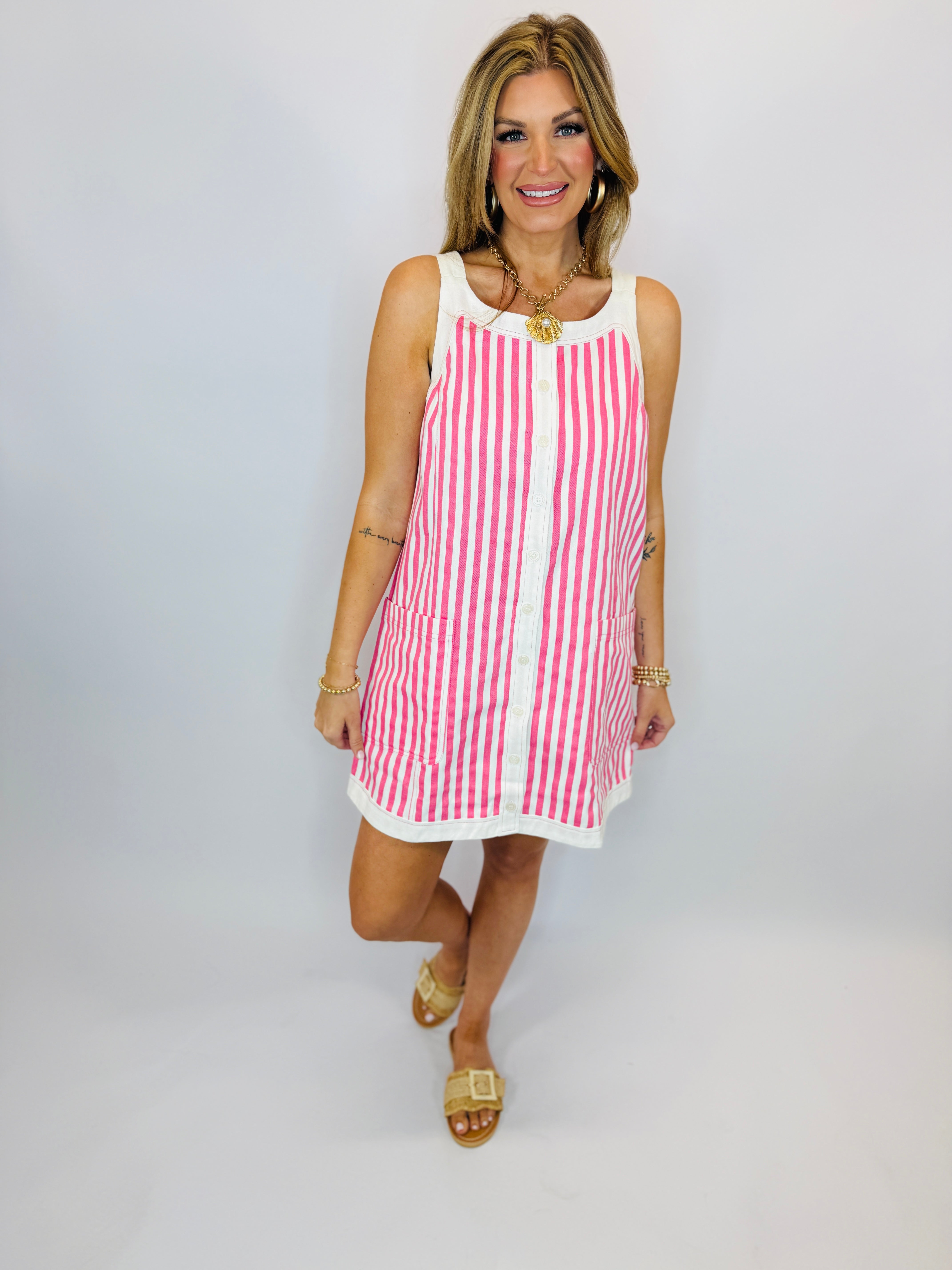 Woman wearing pink and white striped sleeveless mini dress with white trim and gold sandals.