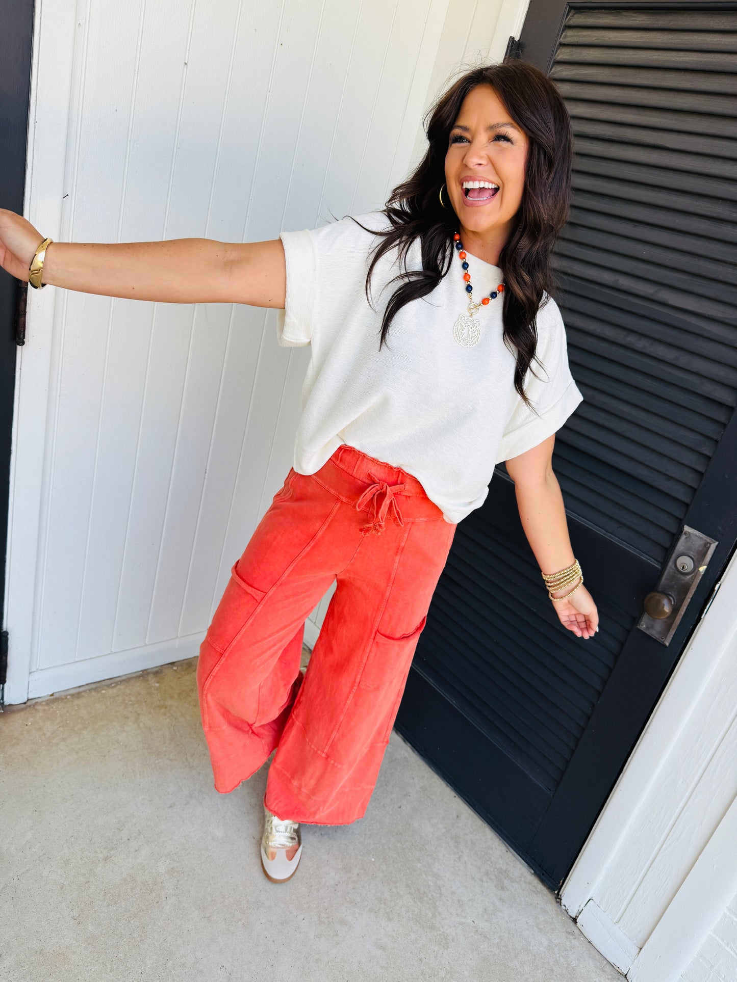 Woman wearing coral wide-leg Jessalyn pants with white top and colorful necklace, standing in doorway