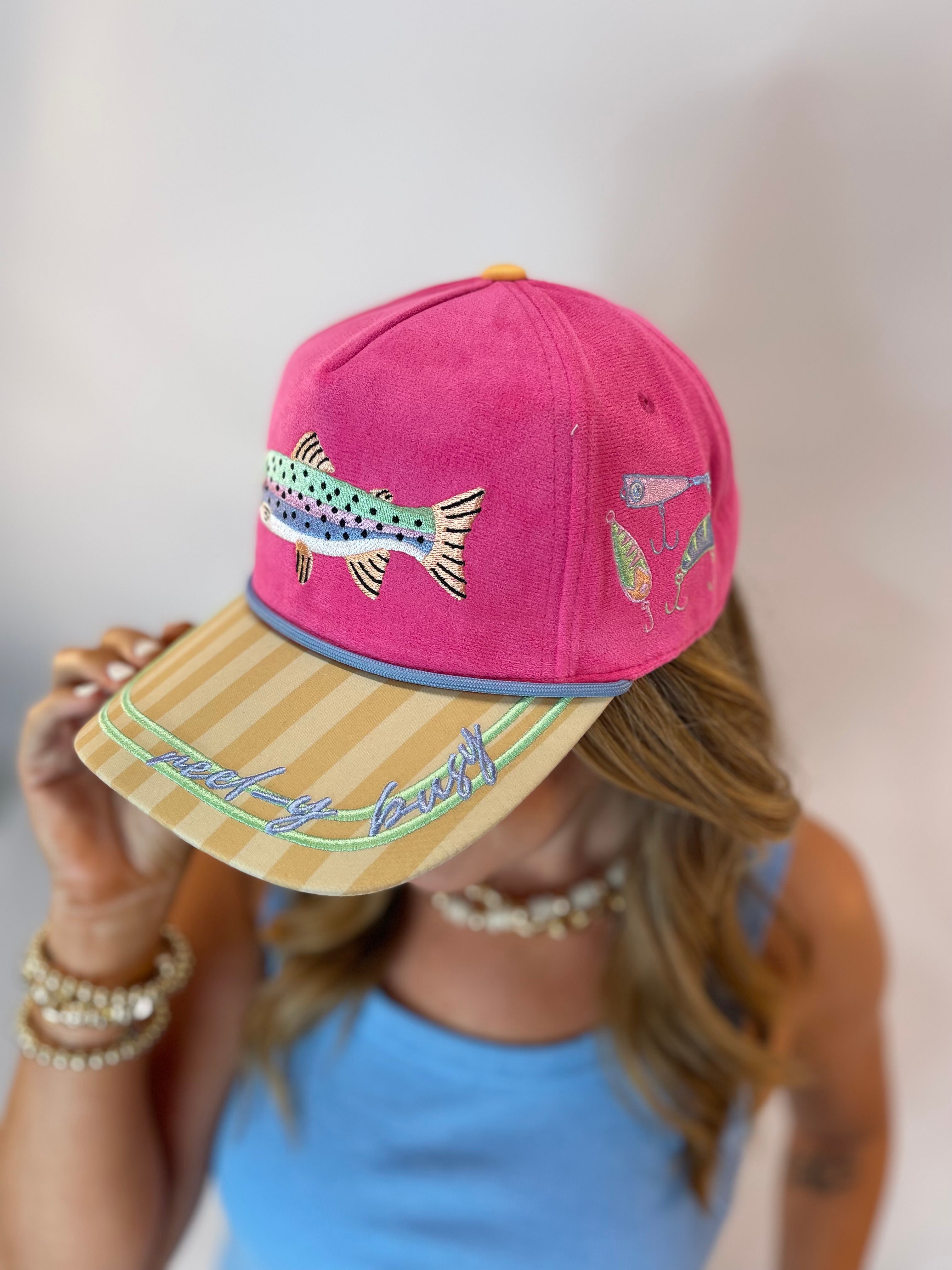 Hot pink suede snapback hat with embroidered rainbow trout and fishing lures, tan striped brim with "Reel-y Busy" script.