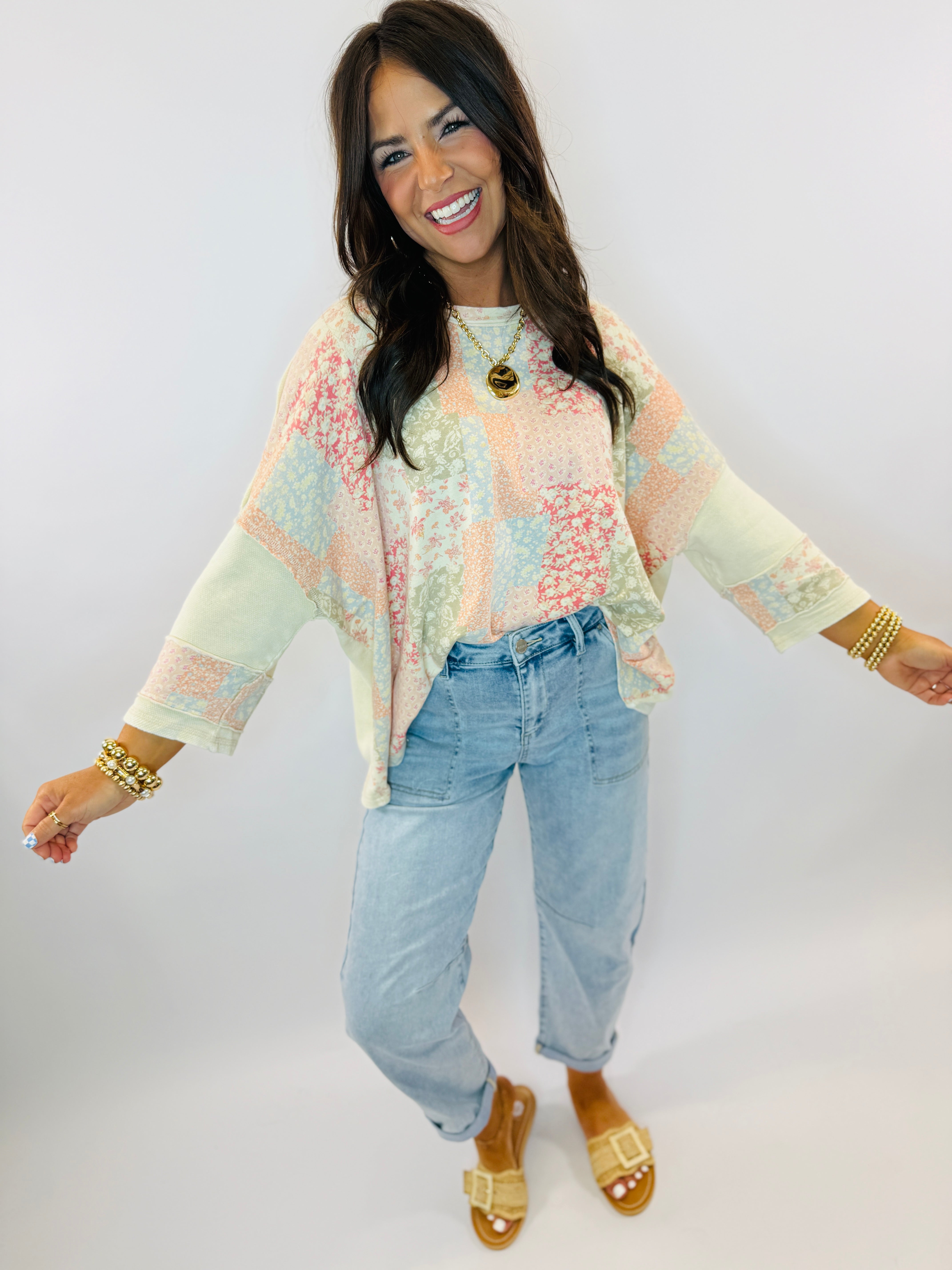 Woman wearing pastel patchwork long-sleeve Ellie top with light blue jeans and gold accessories, smiling against white bac...