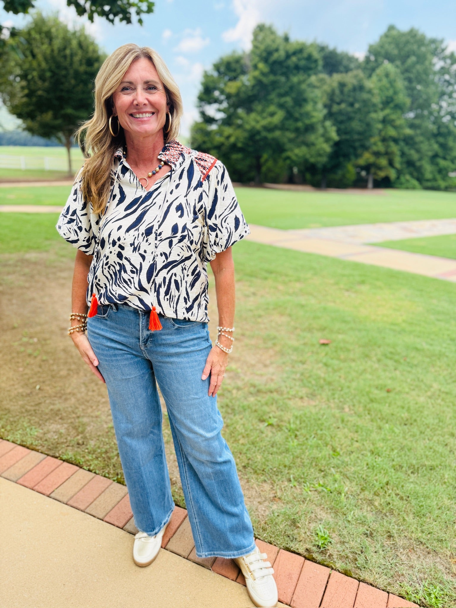 Woman wearing Rita Top in black and white animal print with red tassels, paired with wide-leg jeans.