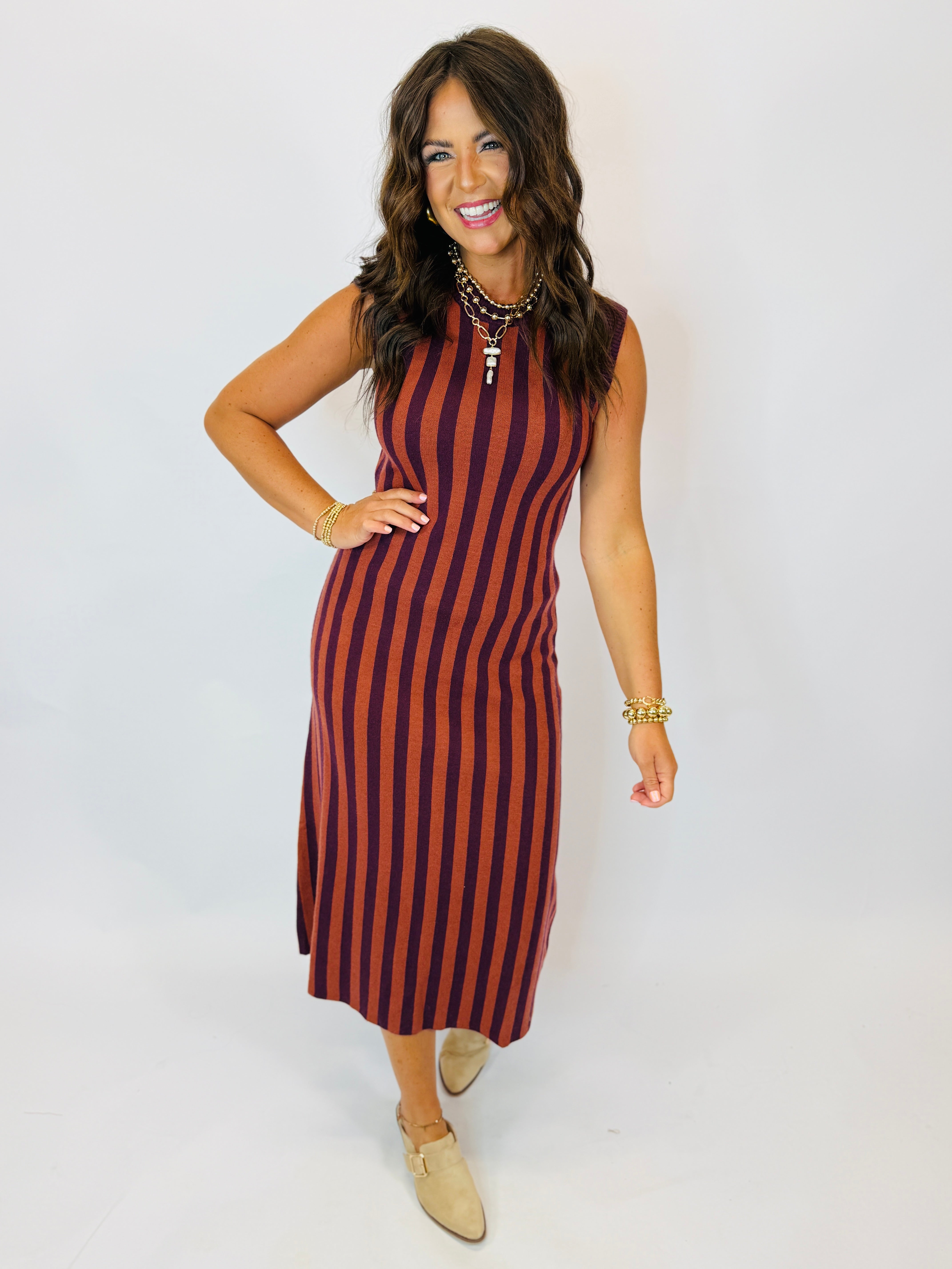 Darcy Dress in rust and burgundy vertical stripes, sleeveless midi length, worn with gold jewelry and tan mules.