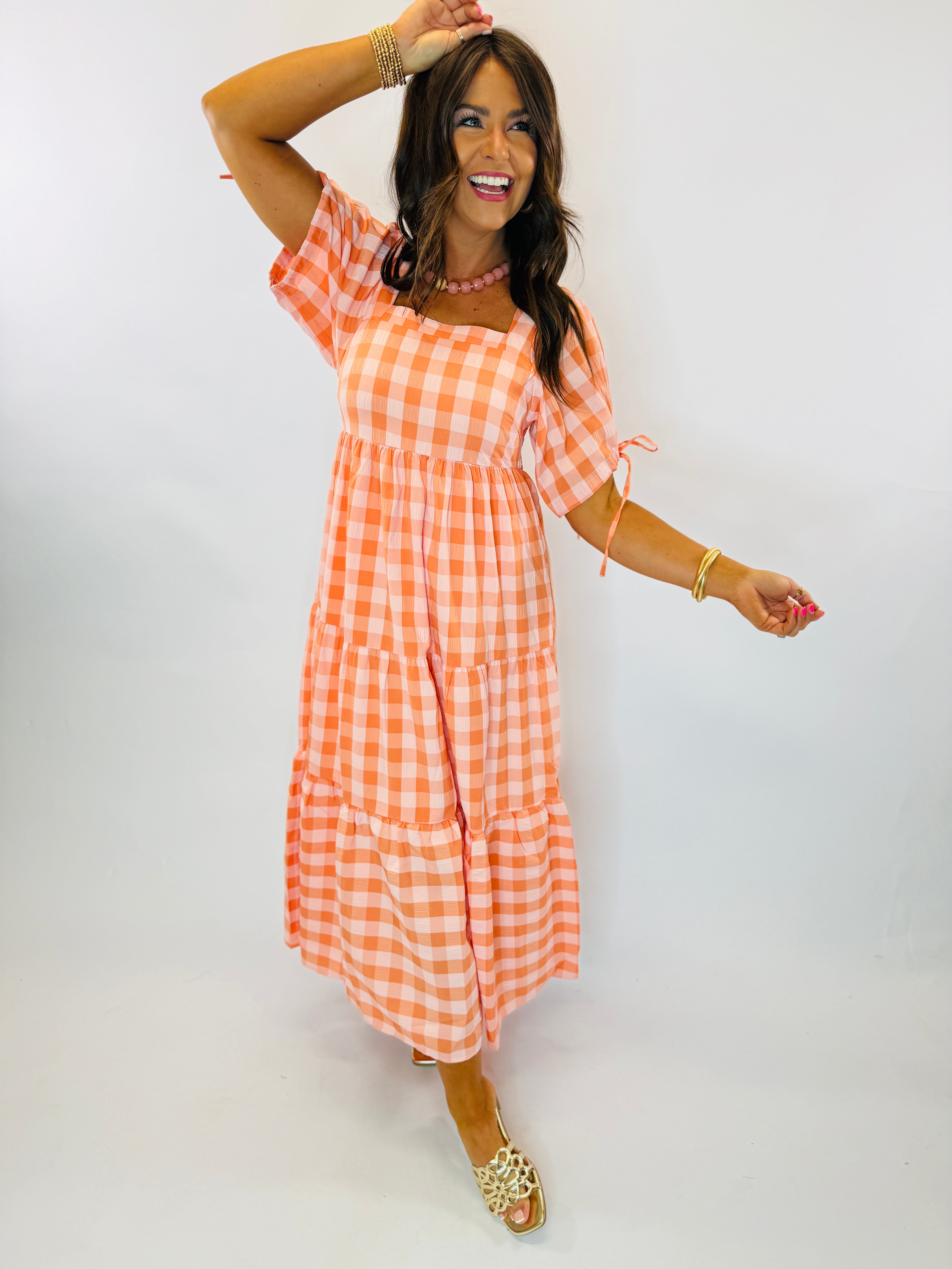 Woman wearing orange and white gingham tiered maxi dress with short puff sleeves and square neckline.