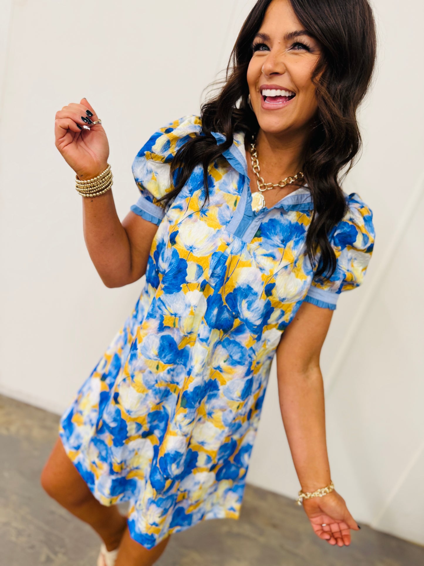 Woman wearing blue and yellow floral print short-sleeve flowy dress with gold jewelry and bracelet