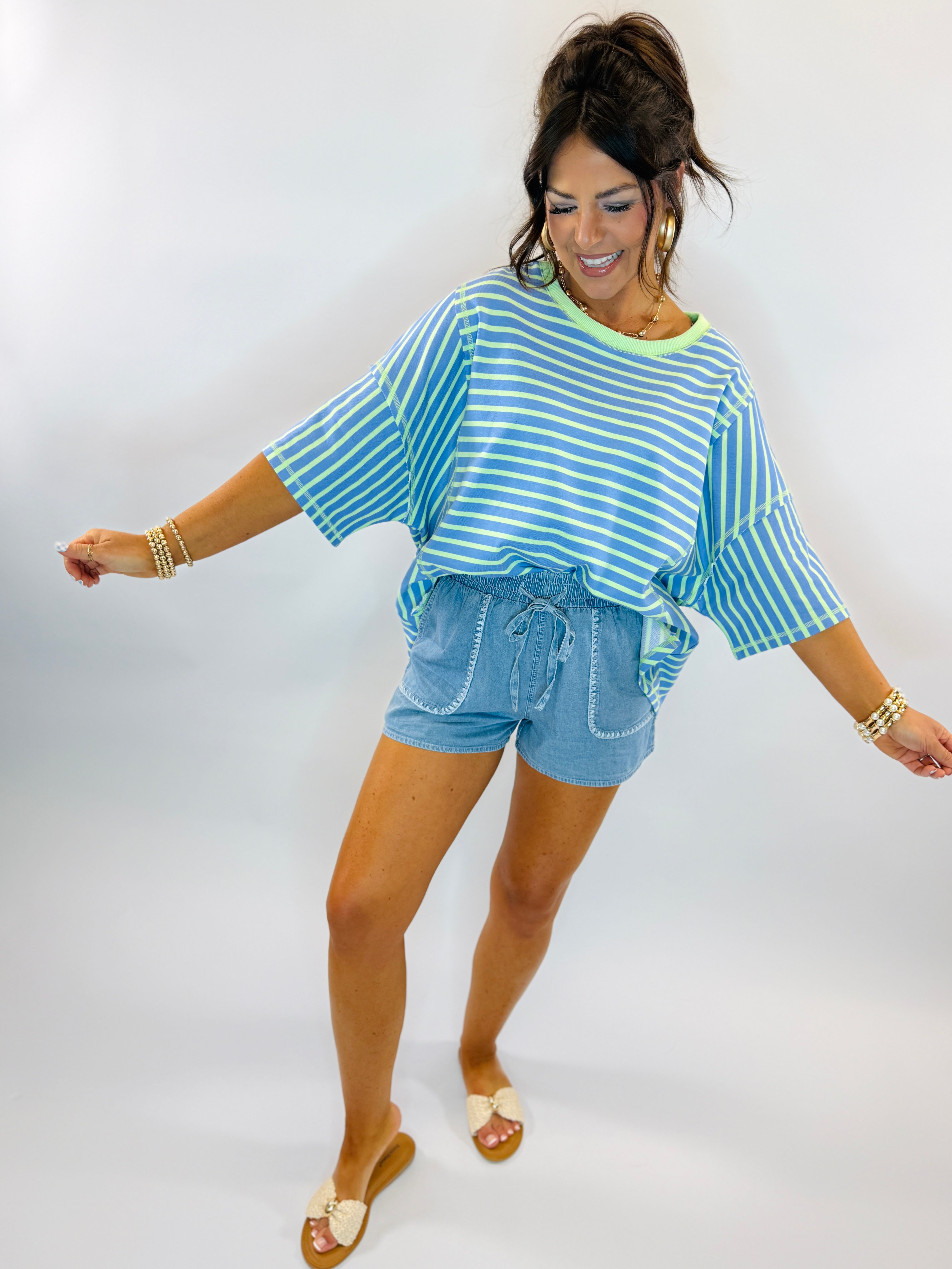 Woman wearing blue and white striped oversized top with light blue denim shorts and sandals