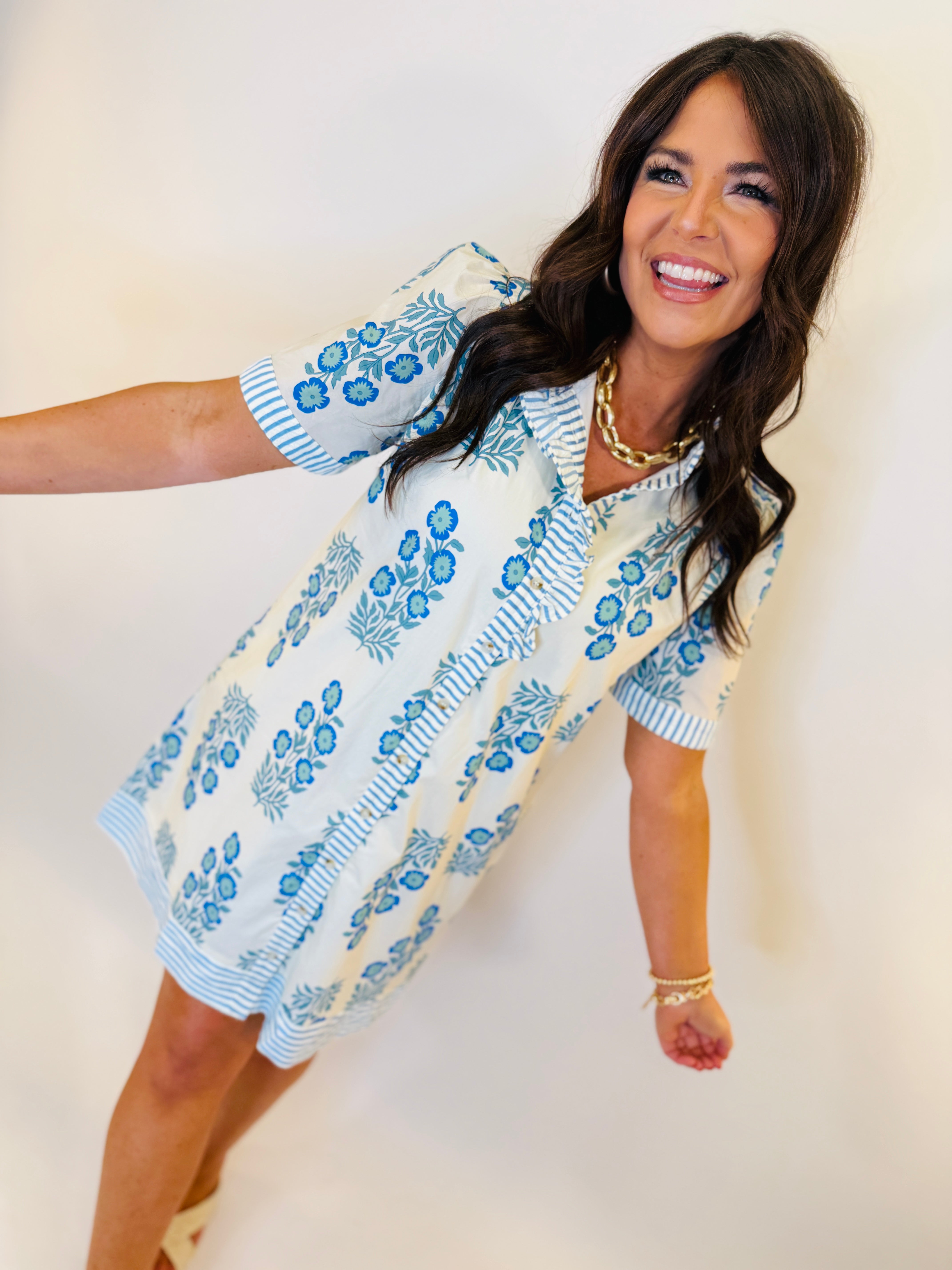 Woman wearing blue and white floral patterned Samira dress with short sleeves, smiling and posing playfully.