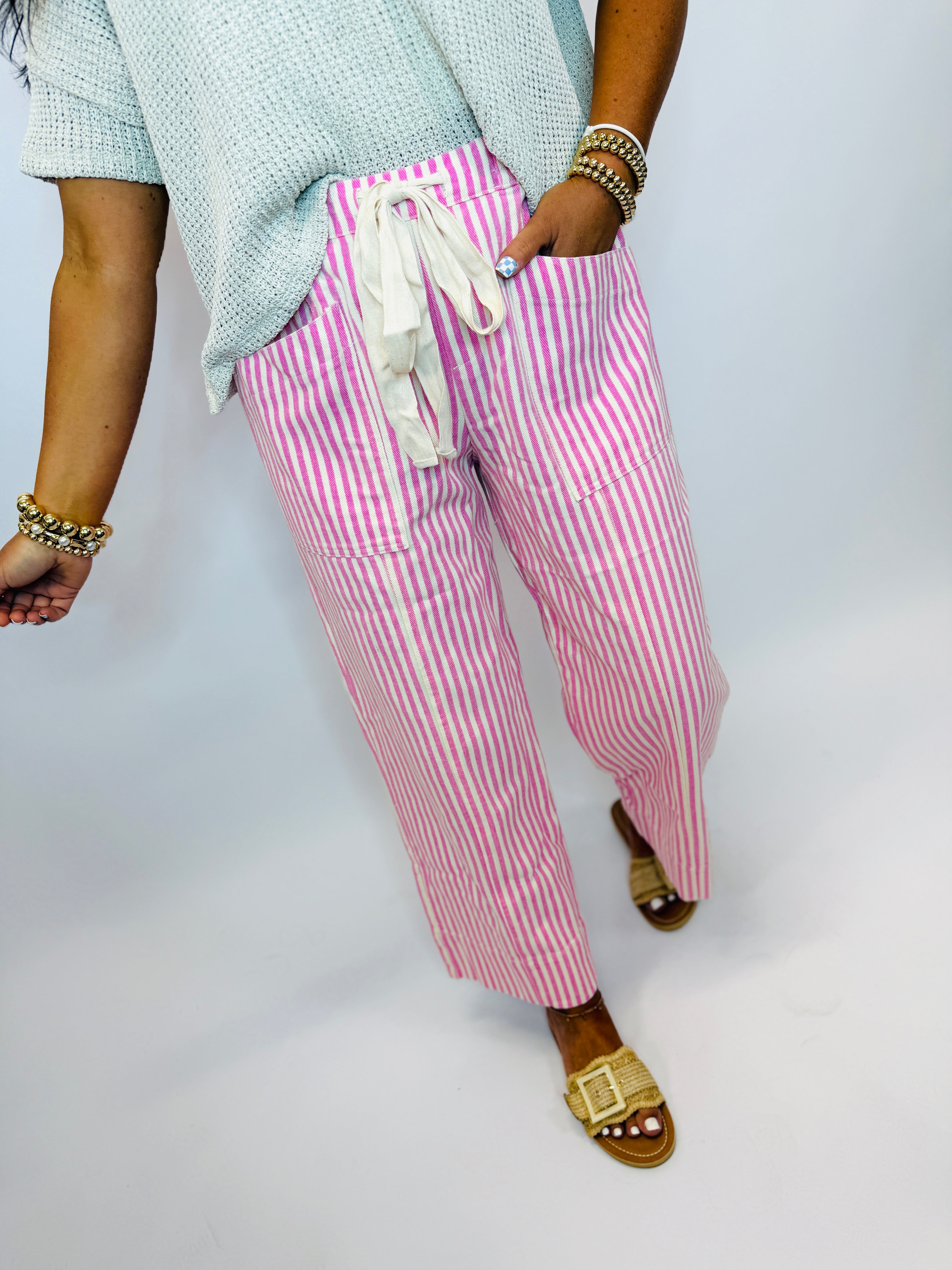 Pink and white striped drawstring pants with front pockets, styled with a light blue knit top and tan sandals.