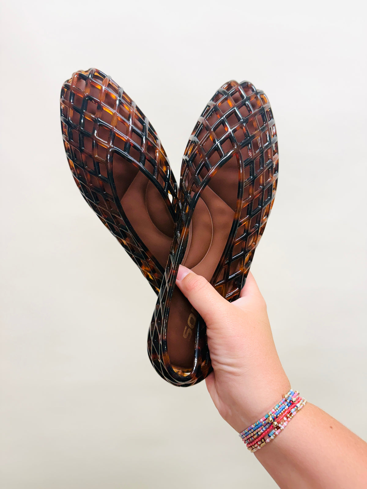 Taylor Jelly Flat in tortoiseshell brown lattice pattern, held up by hand wearing colorful beaded bracelets.
