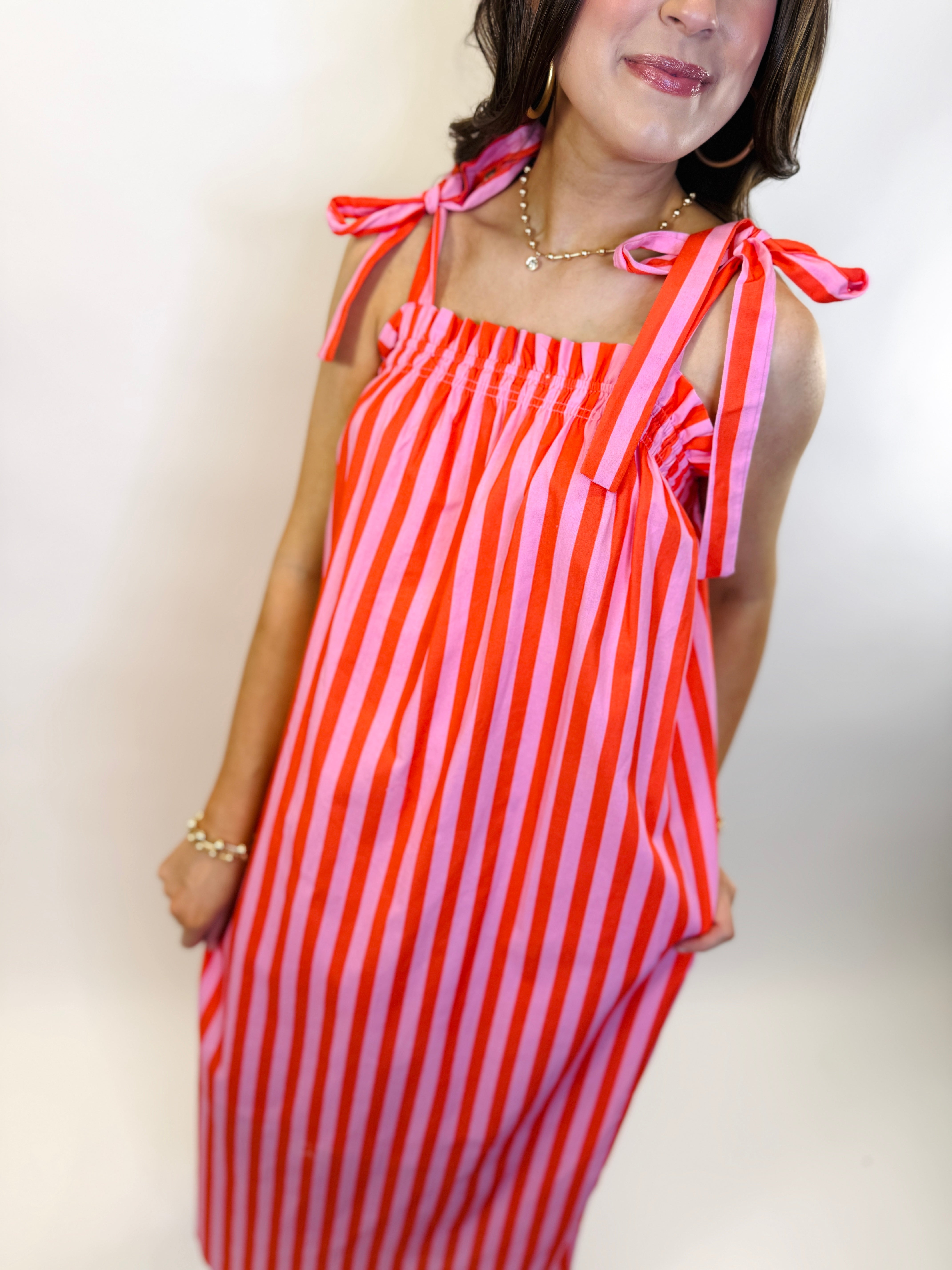 Woman wearing red and pink striped midi dress with tie shoulder straps and ruffle detail
