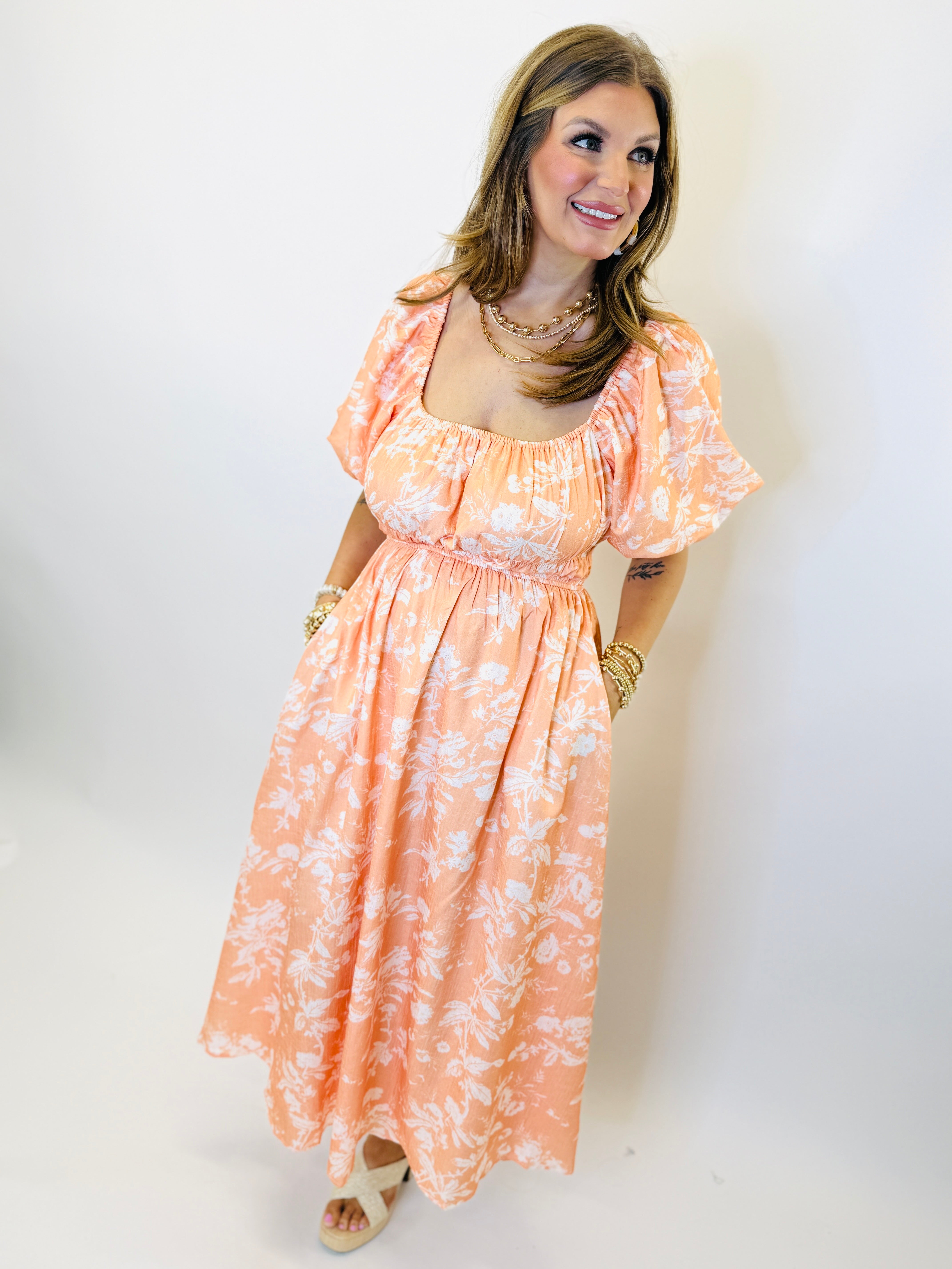 Woman wearing coral floral print midi dress with puffed sleeves, smocked waist, and scoop neckline