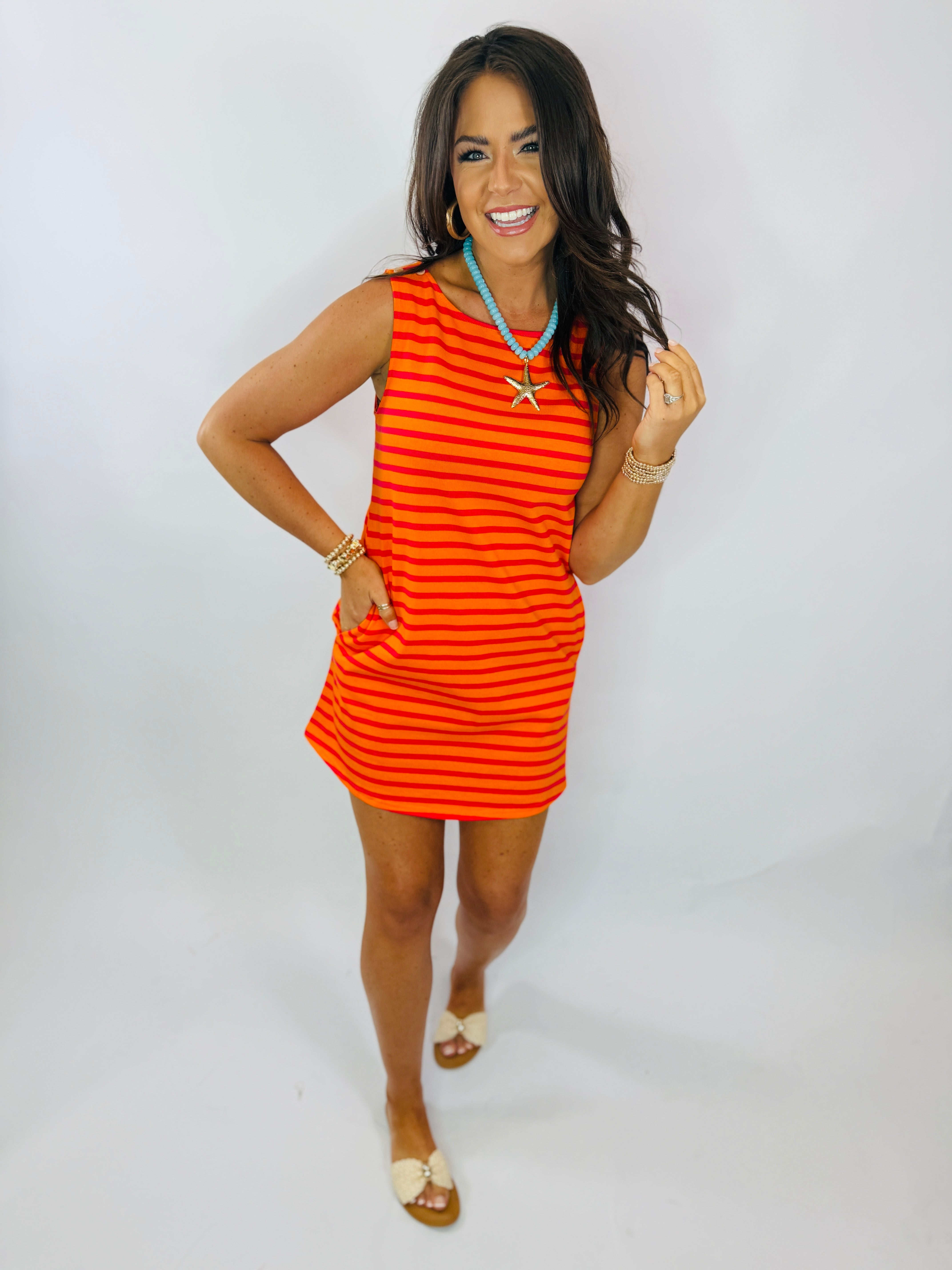 Woman wearing orange and red striped sleeveless mini dress with turquoise necklace and gold accessories