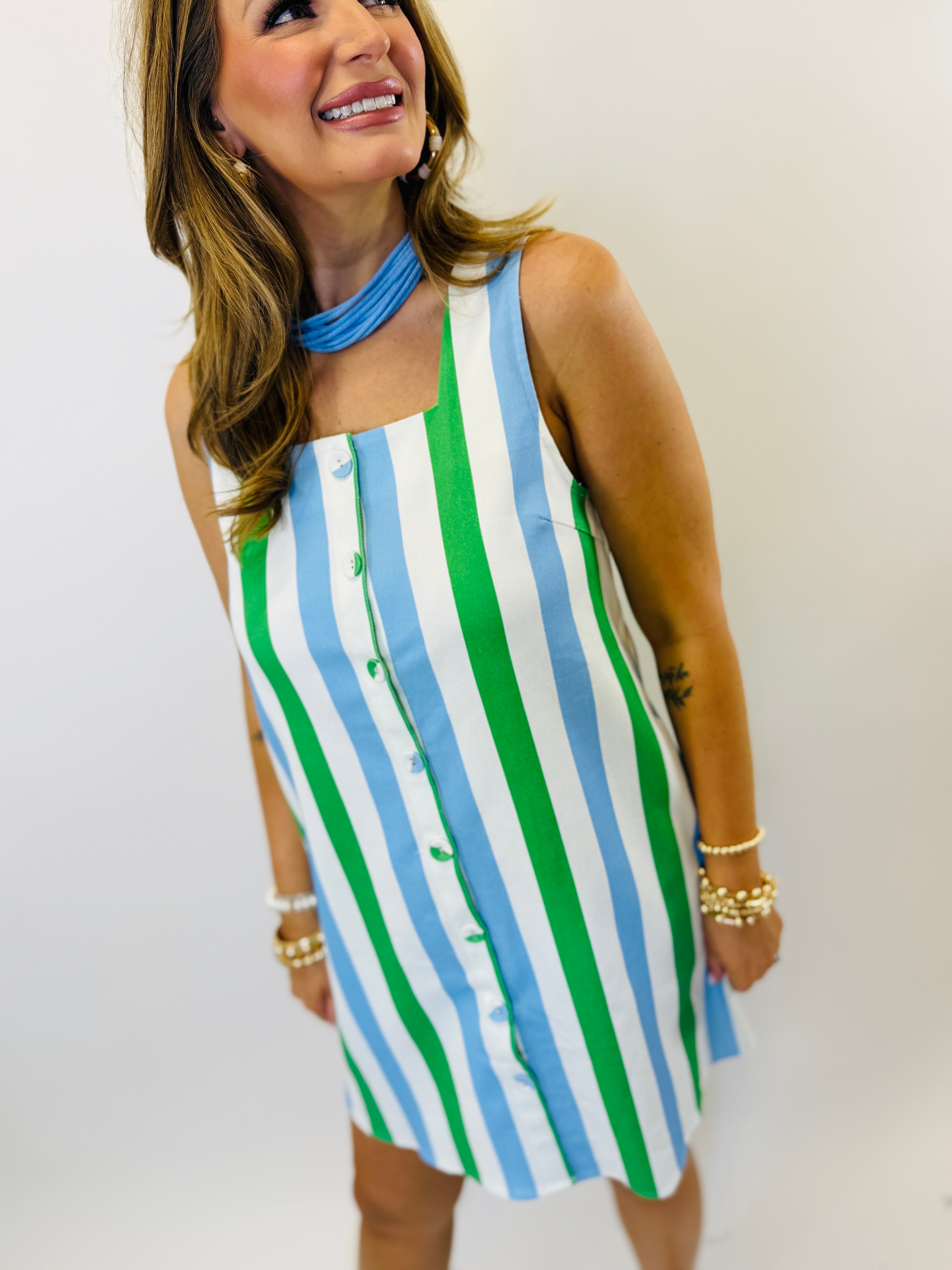 Woman wearing blue, white and green striped sleeveless button-front halter dress with matching choker necklace.