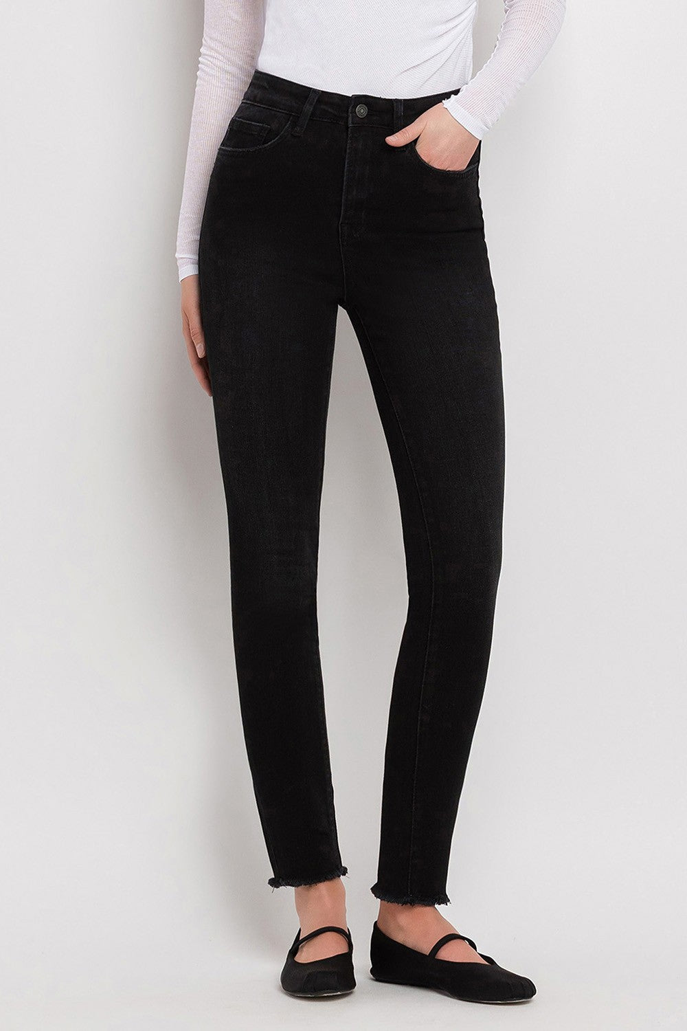 Black high-waisted skinny jeans with frayed hem worn with white long-sleeve top and black flats