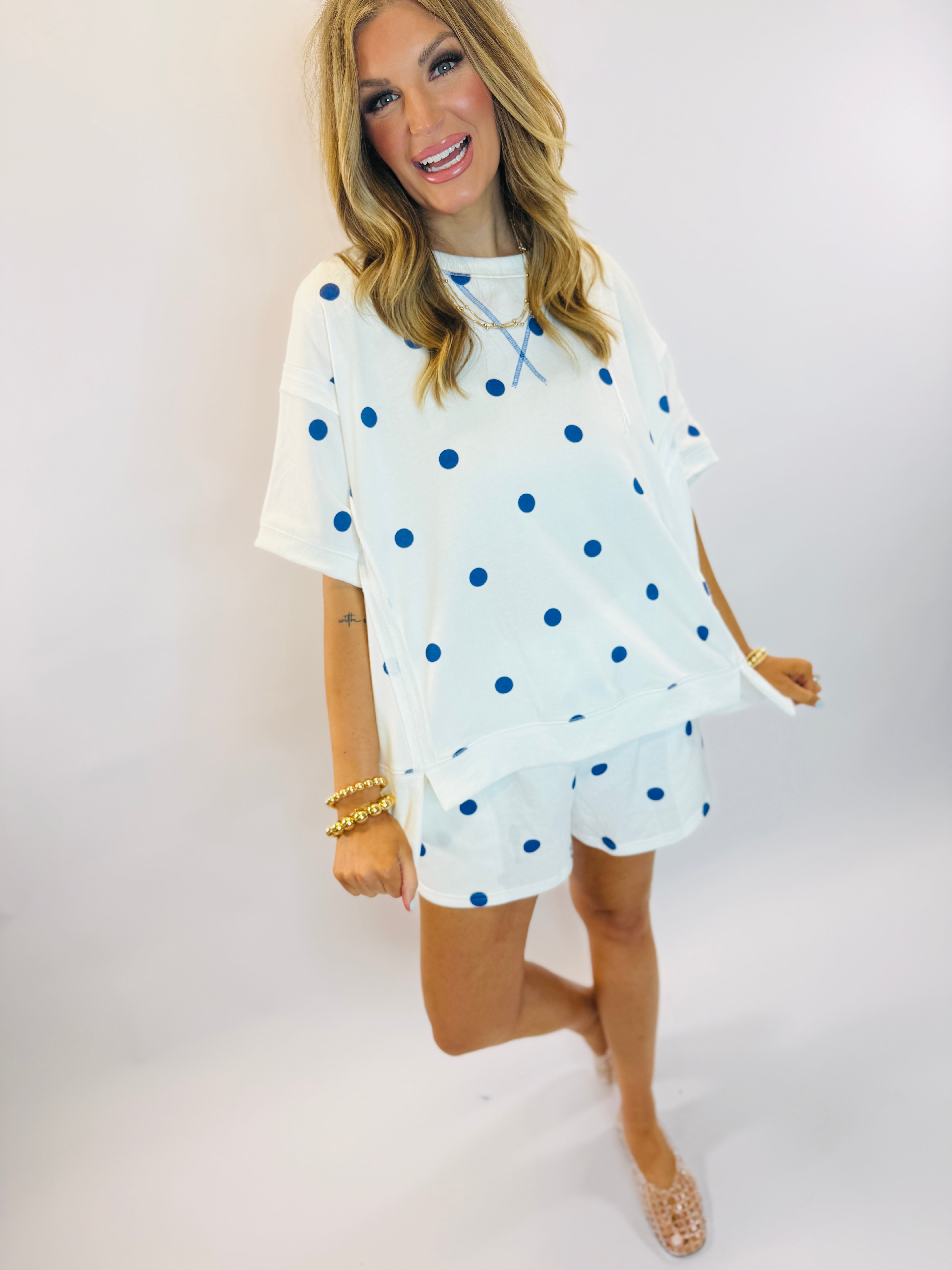 Woman wearing white polka dot matching set with blue dots, featuring oversized top and shorts