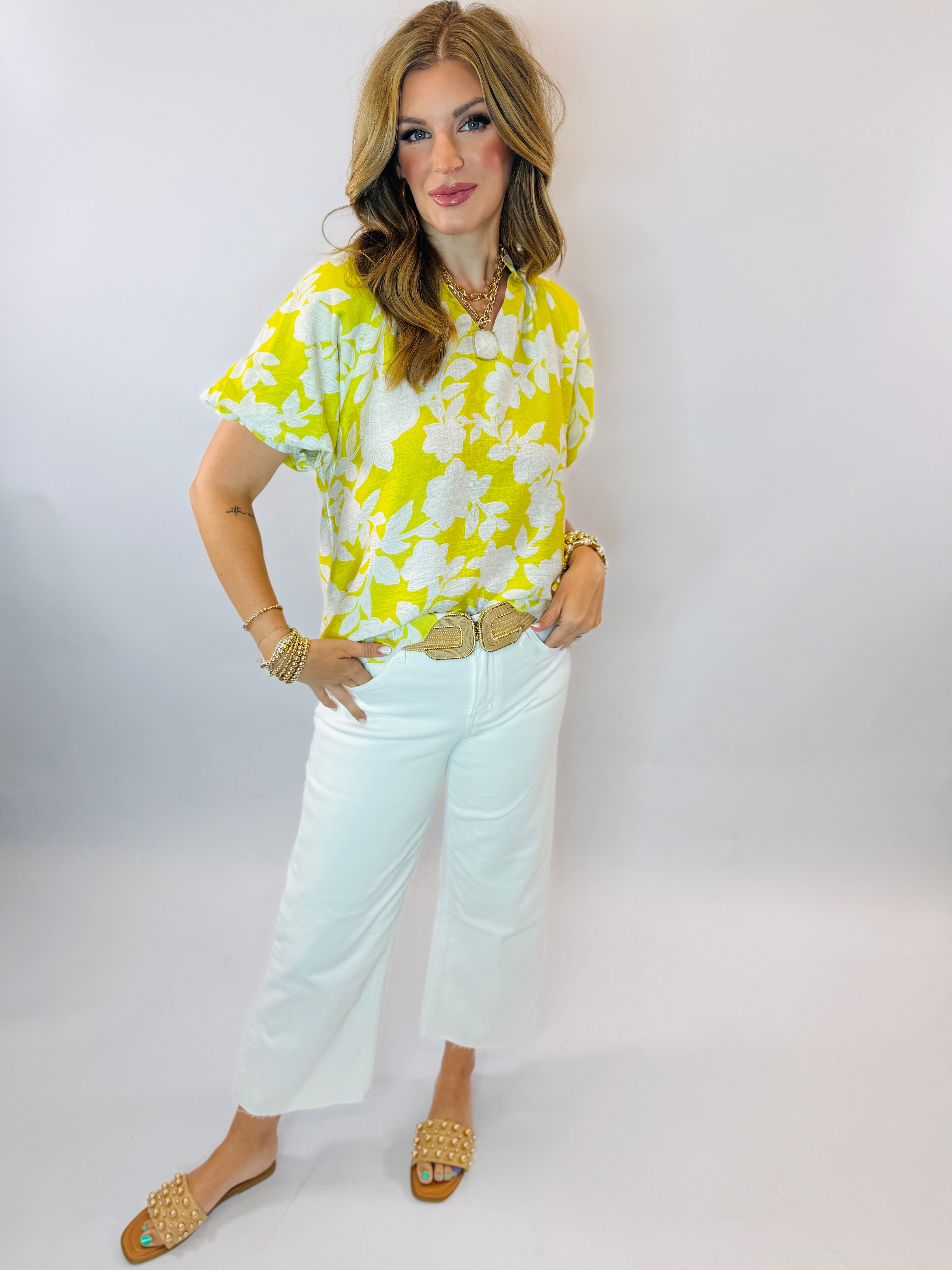 Woman wearing bright yellow floral print short-sleeve blouse with white cropped jeans and gold accessories