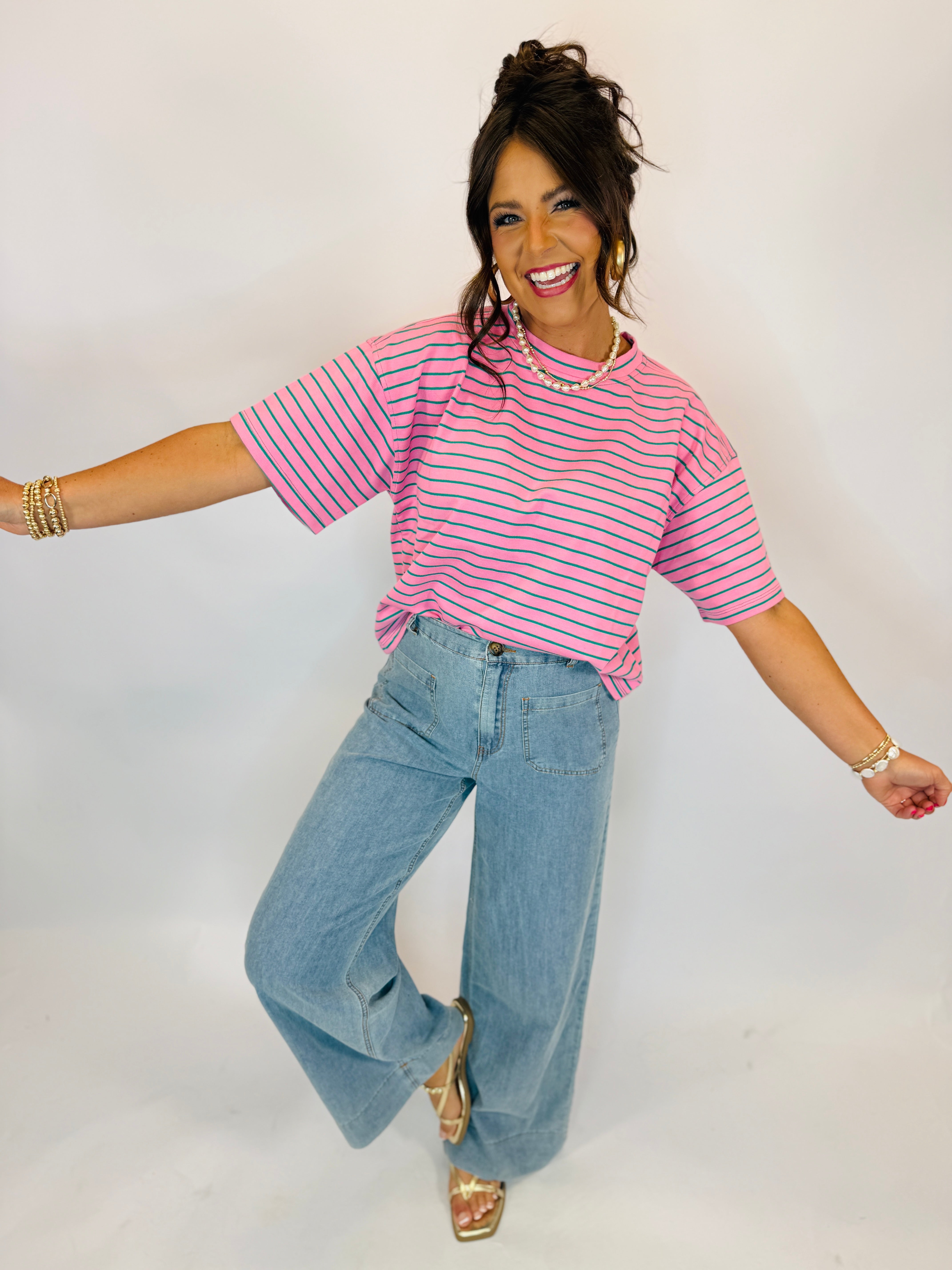 Woman wearing pink and green striped short-sleeve Taylor Top with wide-leg light wash jeans.