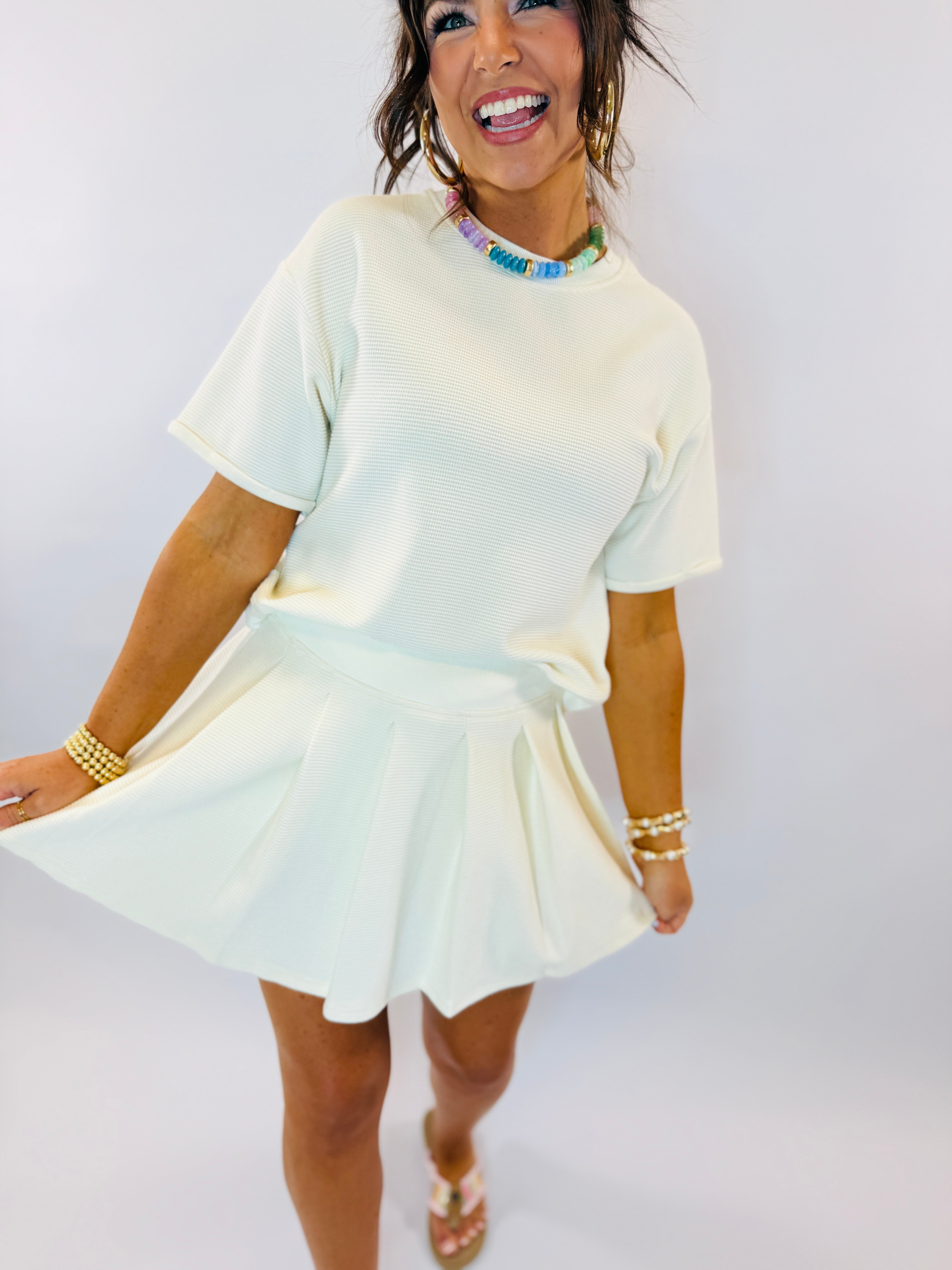 Woman wearing light mint green matching knit top and skort set with colorful beaded necklace and gold jewelry.