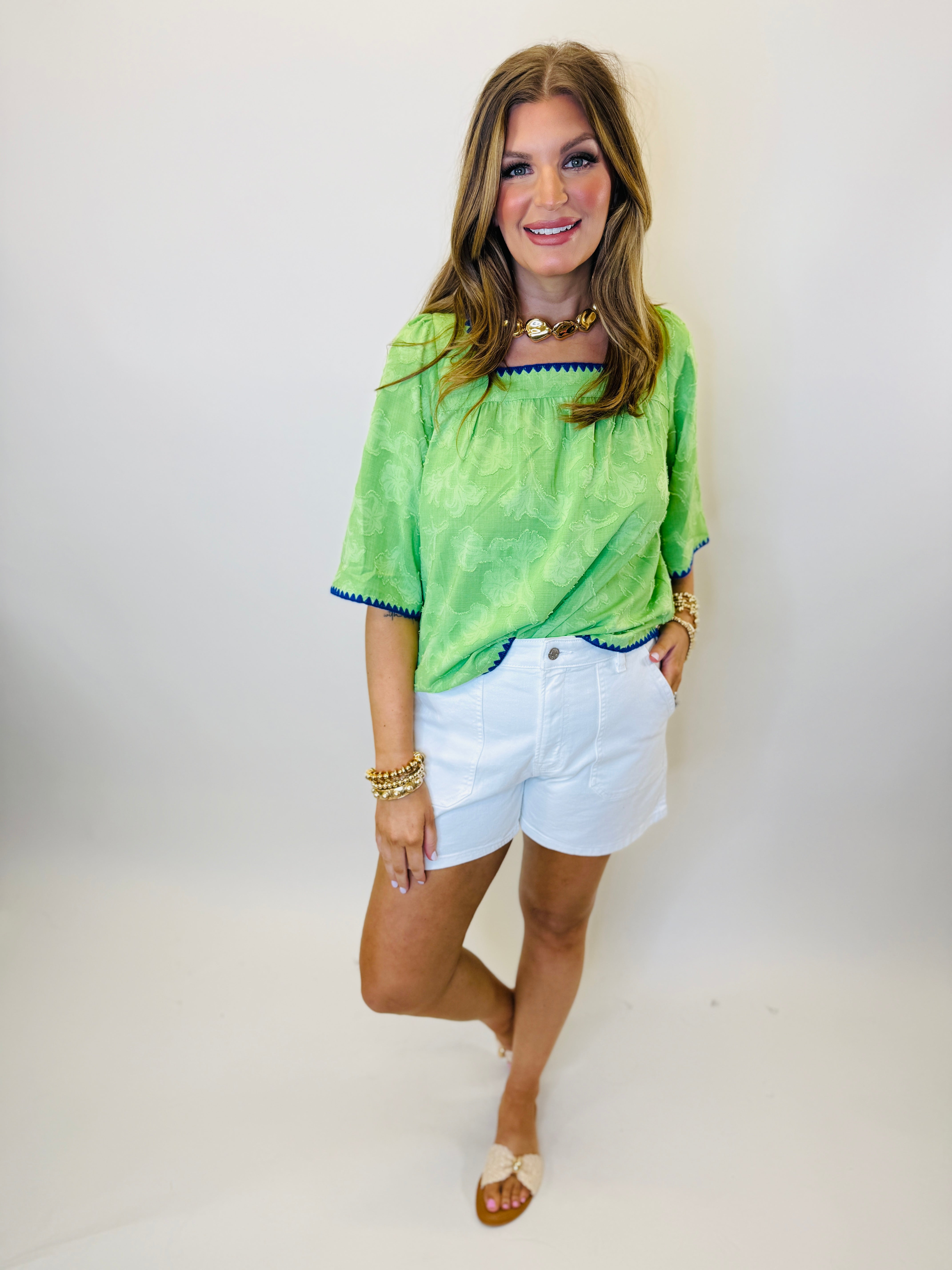 Woman wearing white Walker shorts with green top and gold jewelry, standing against neutral background