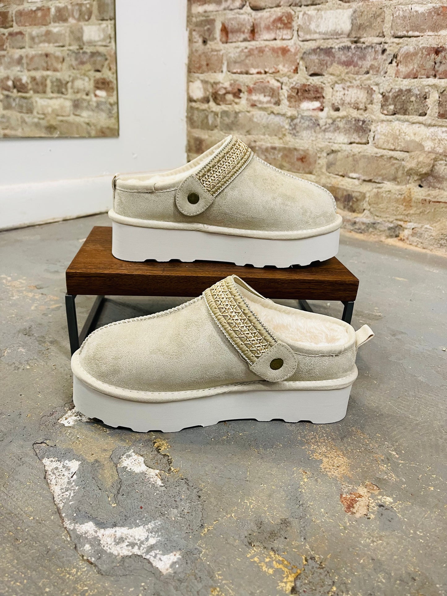 Beige suede platform slippers with gold chain detail and white chunky soles displayed on wooden bench.