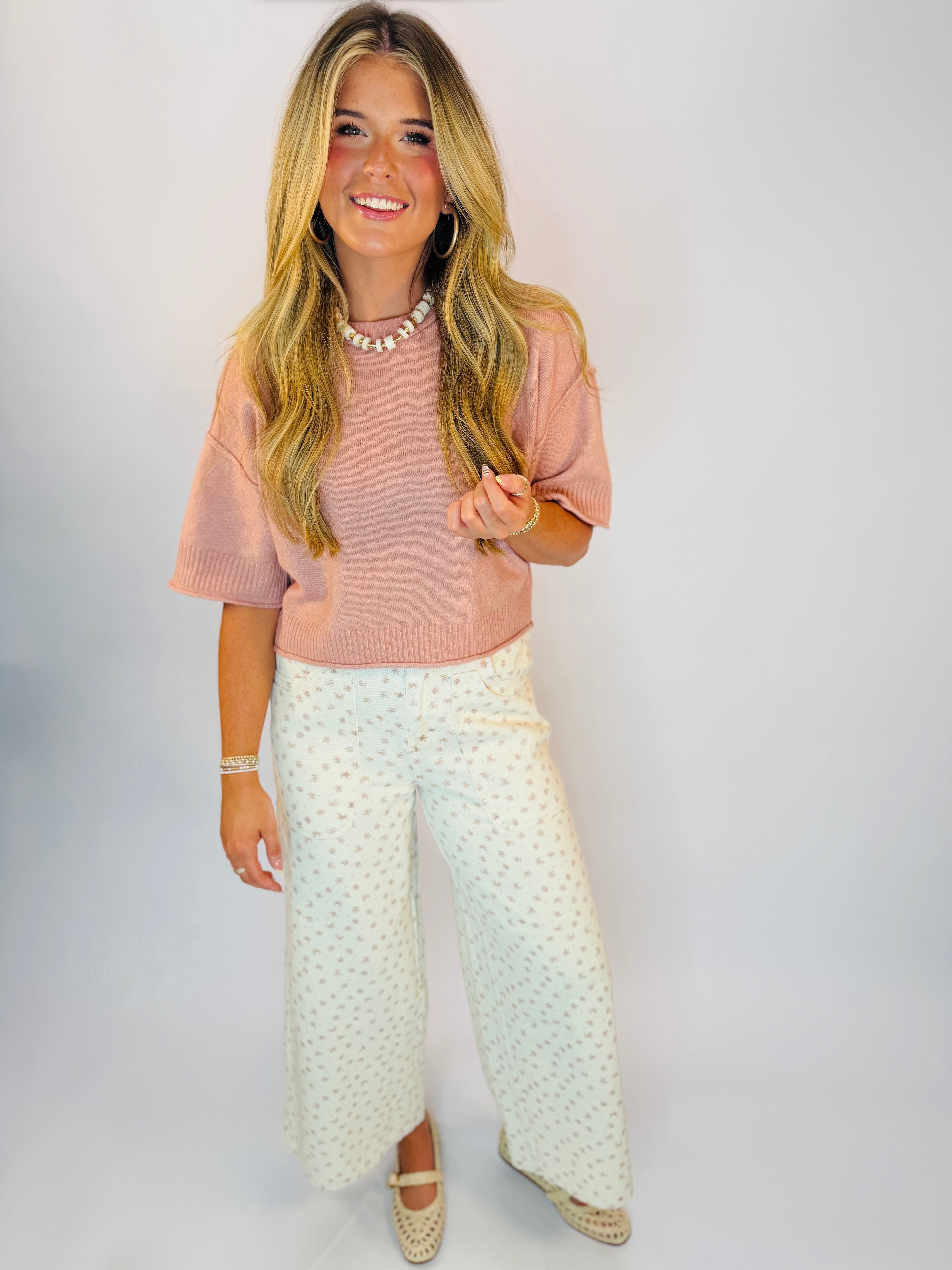 White wide-leg Zori Pants with small floral print, styled with a pink crop sweater and woven flats.