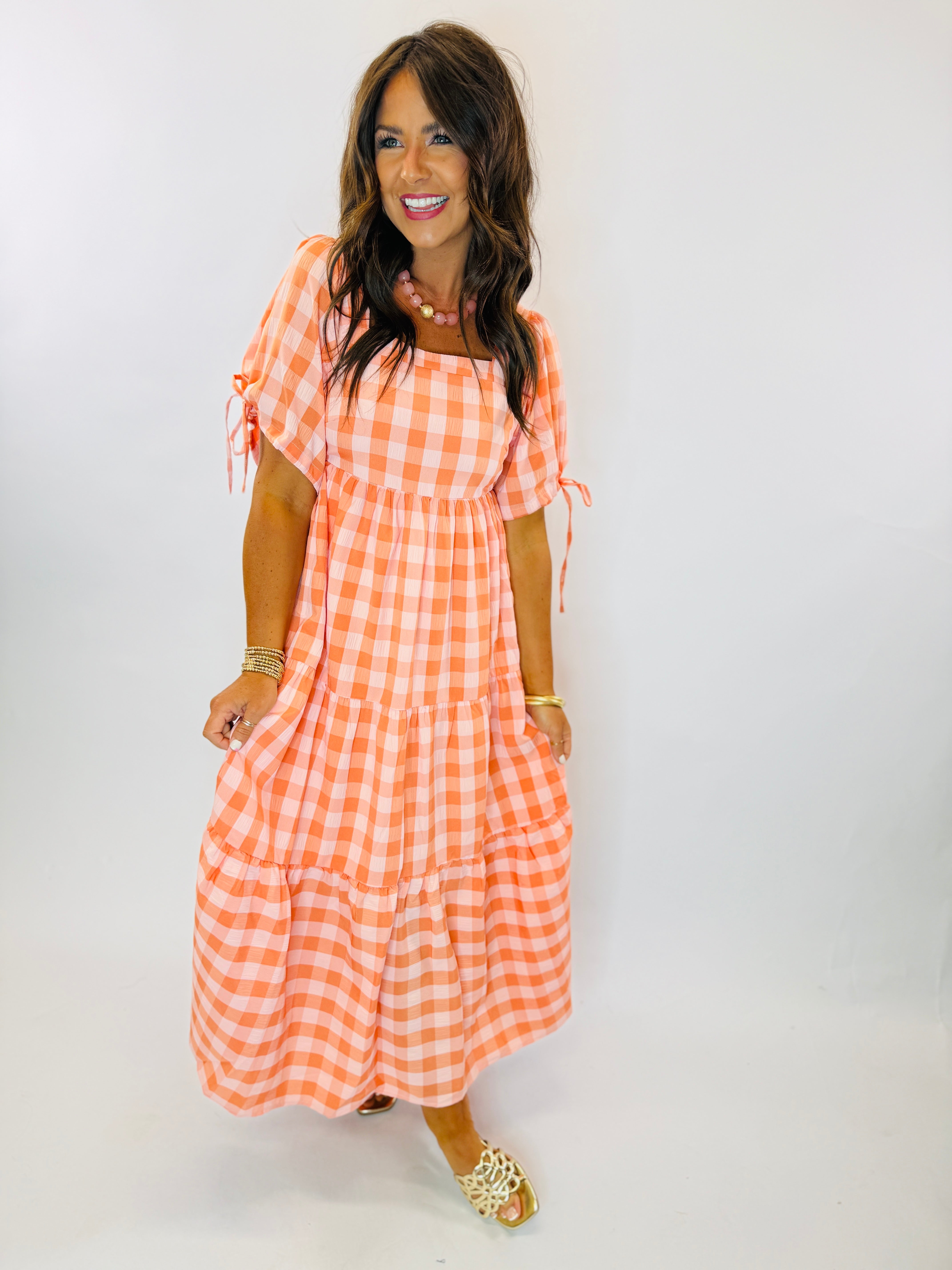 Woman wearing orange and white gingham tiered maxi dress with puff sleeves and tie details.